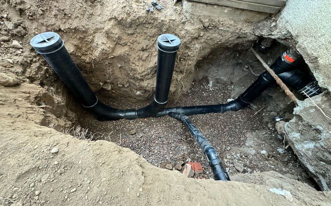 Underground plumbing pipes and vents installed in a dirt trench at a construction site