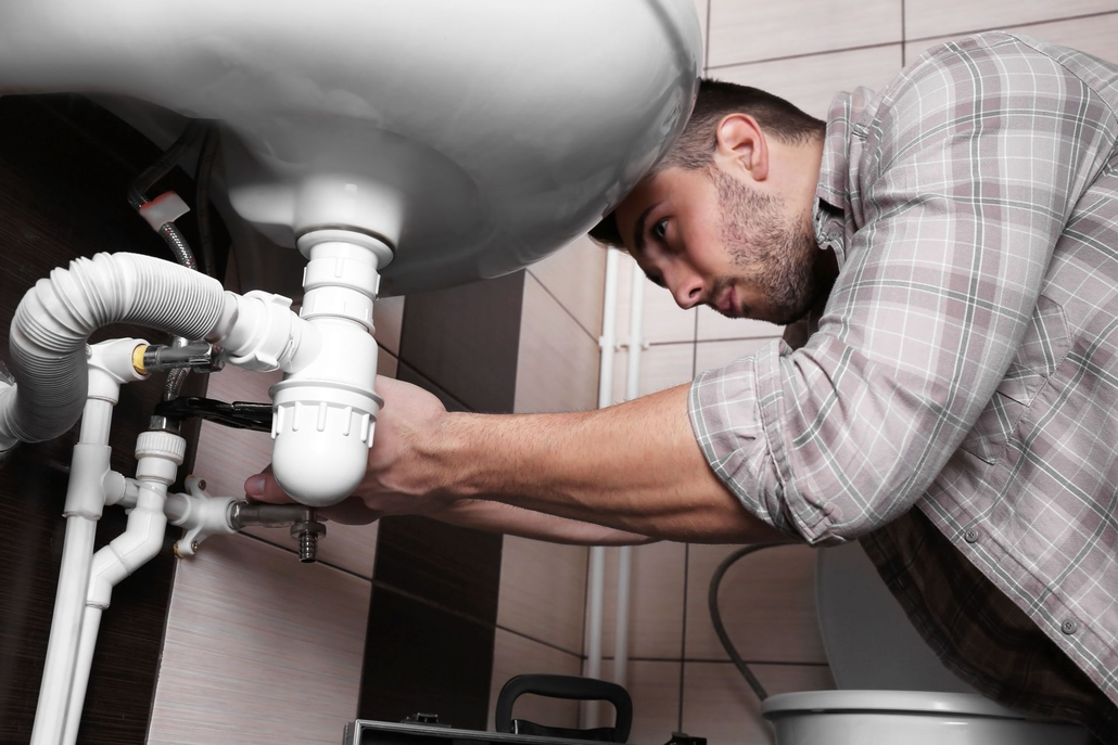 Plumber repairing pipes under a bathroom sink with a wrench