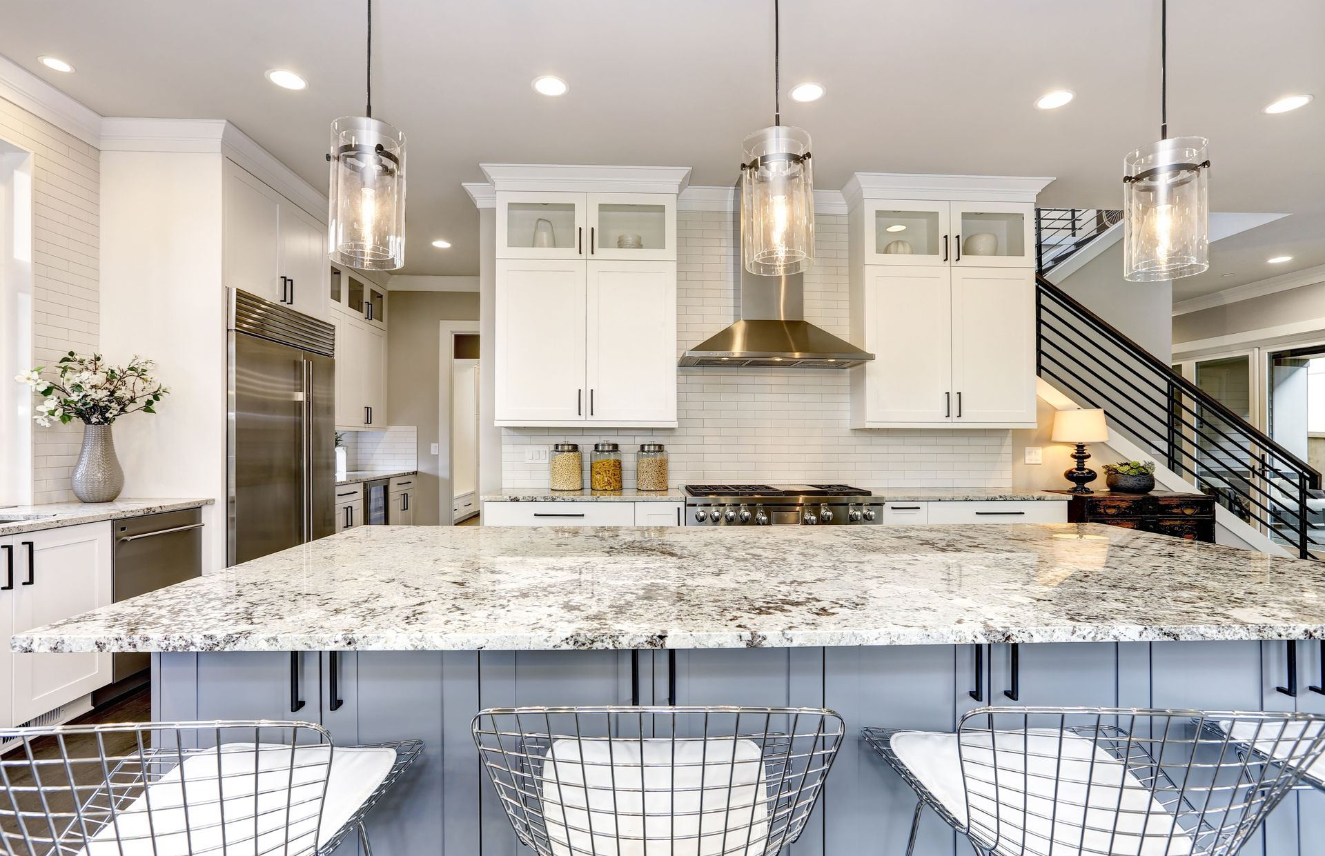 Modern kitchen with white cabinets, granite countertop, stainless steel appliances, and hanging lights.
