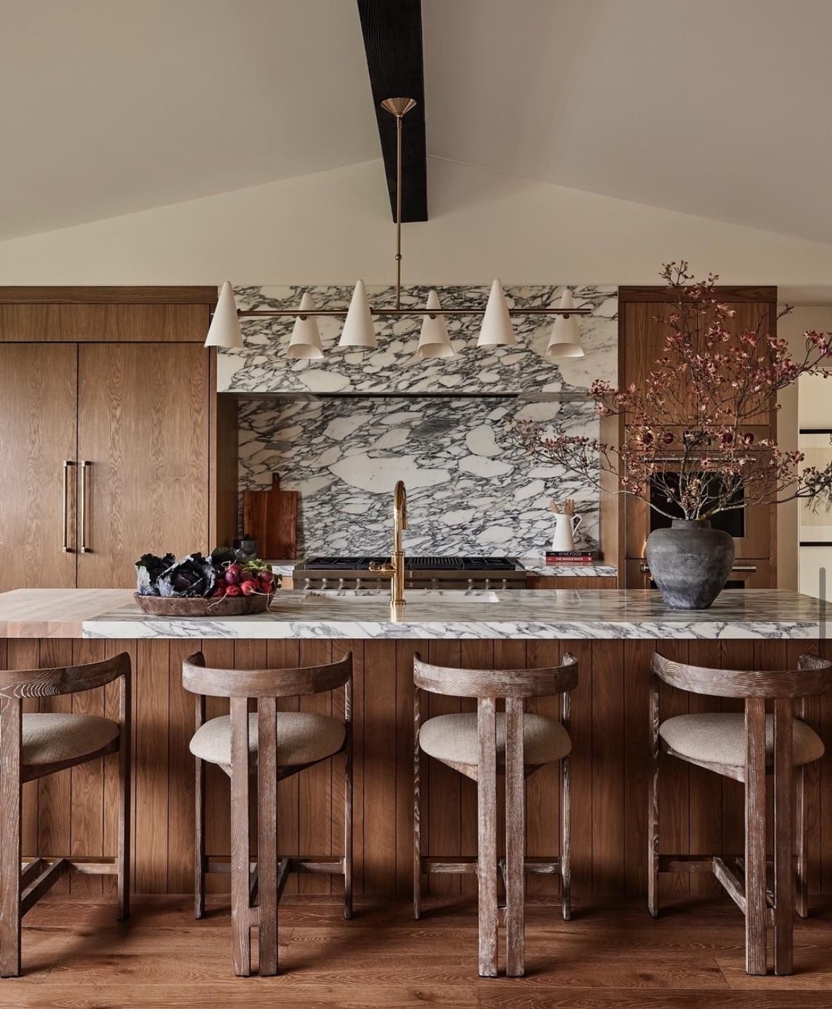 Kitchen with marble backsplash, wood cabinets, island with stools, and beige walls.