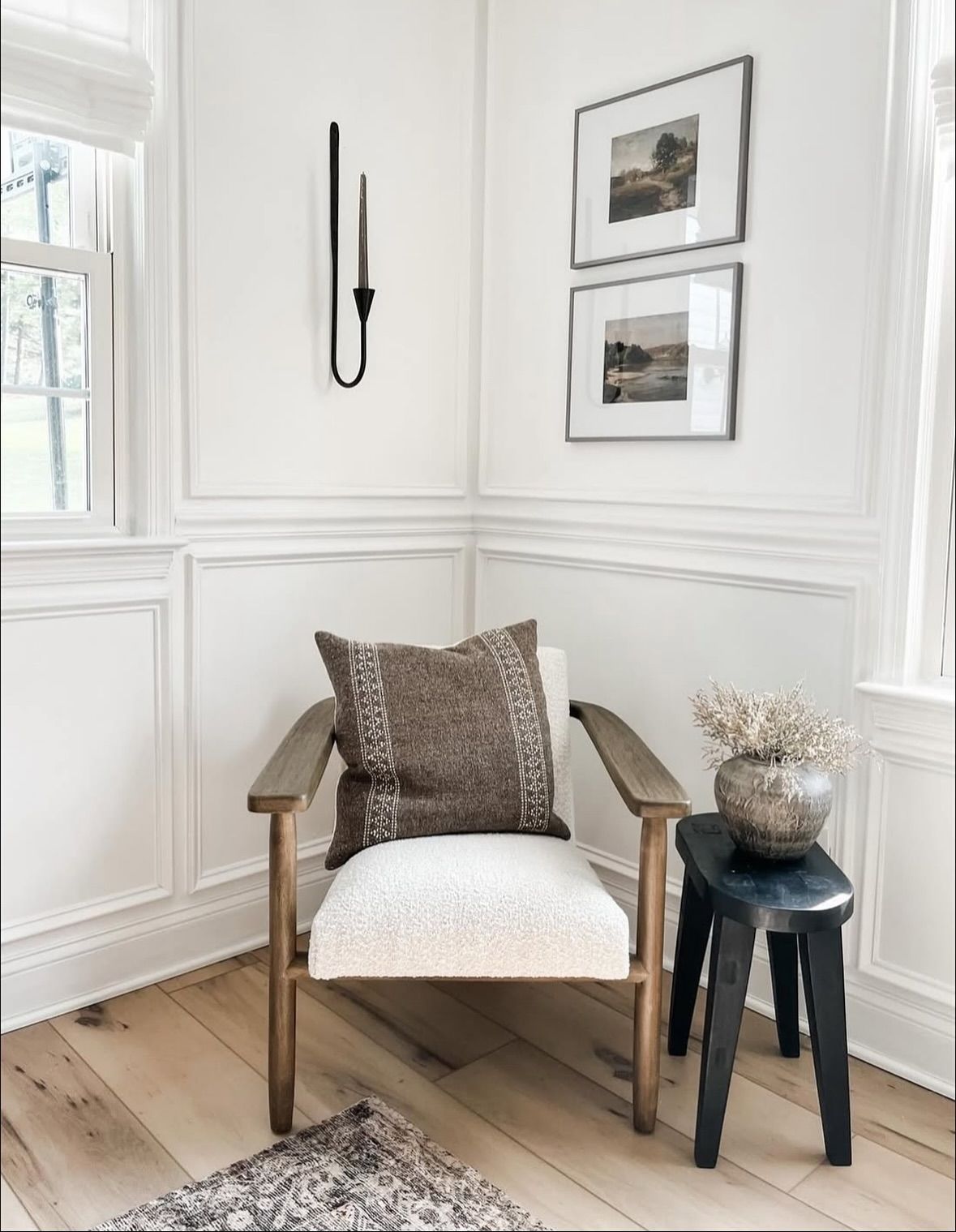 Cozy corner with a wooden armchair, framed artwork, and a black candle holder.