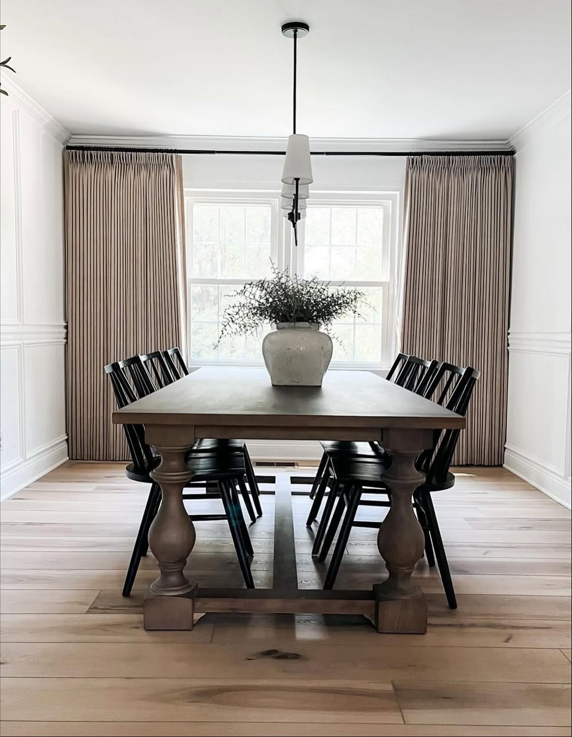 Dining room with a wooden table, black chairs, tan curtains, and a vase of flowers.