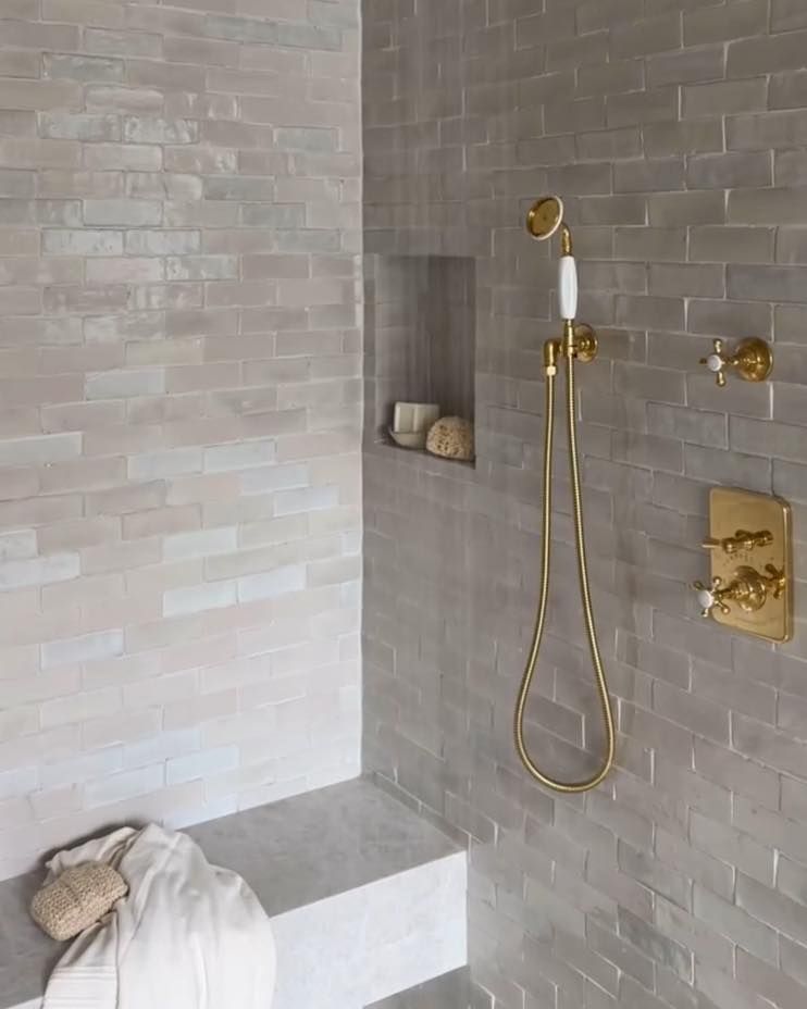 Bathroom with gray brick-like tile. Gold shower fixtures and built-in bench.