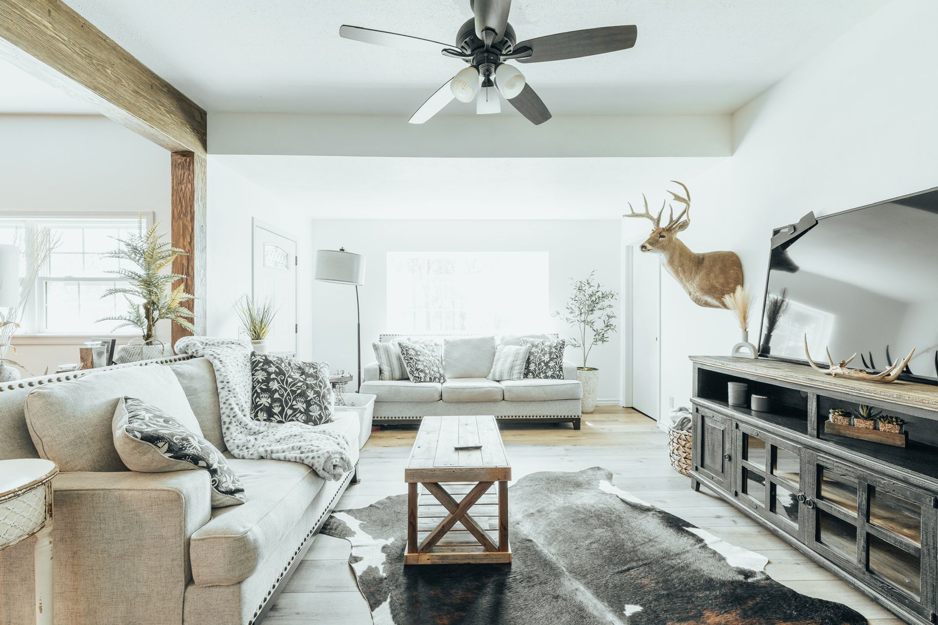 Living room with couches, TV, deer head mount, and cowhide rug.