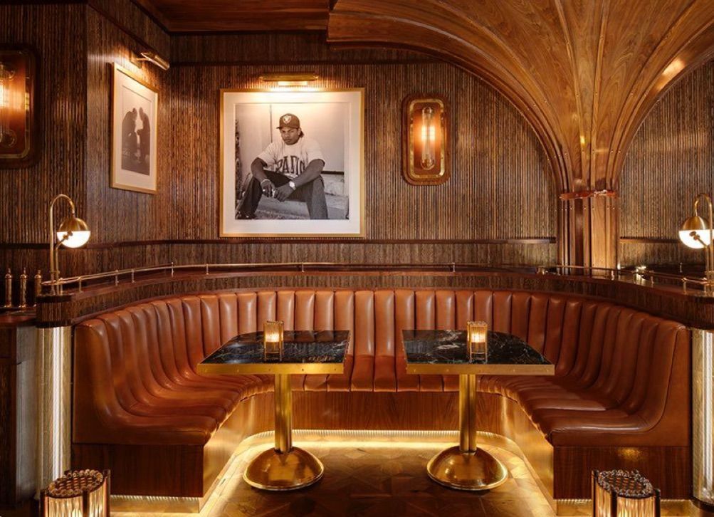 Lounge area with tan armchairs, lamps, and a view of greenery through large windows.