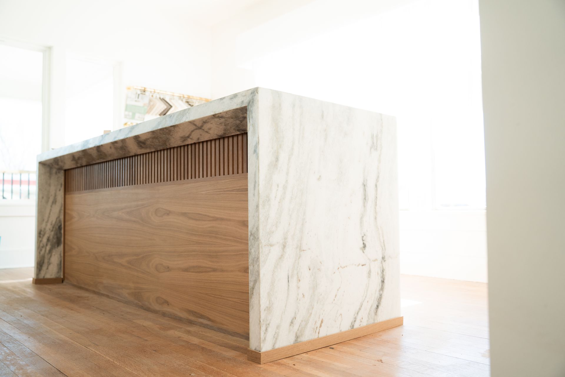 Marble-topped kitchen island with wooden accents on a light wood floor in a bright room.