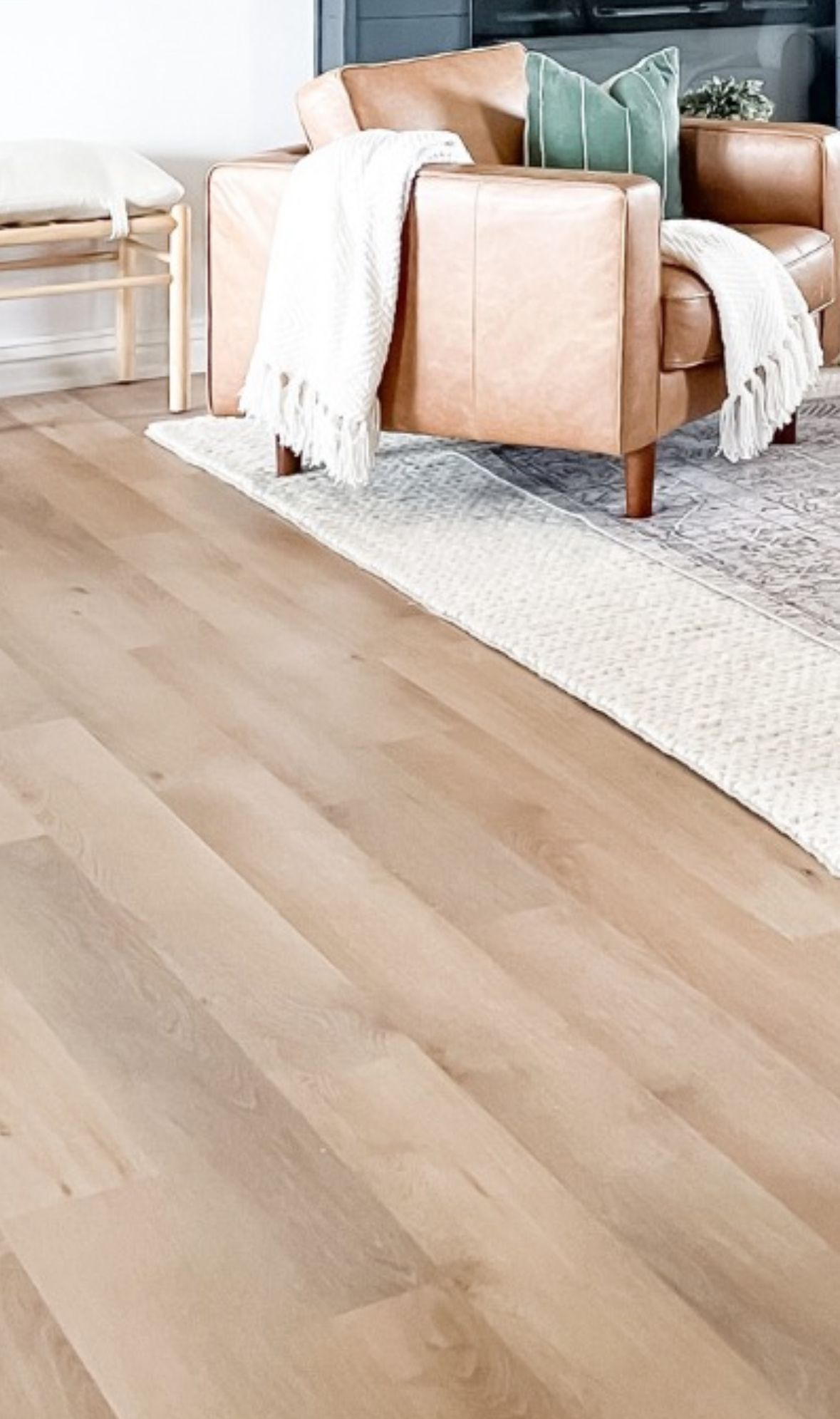 Light brown hardwood floor, with tan leather armchair and a cream blanket.