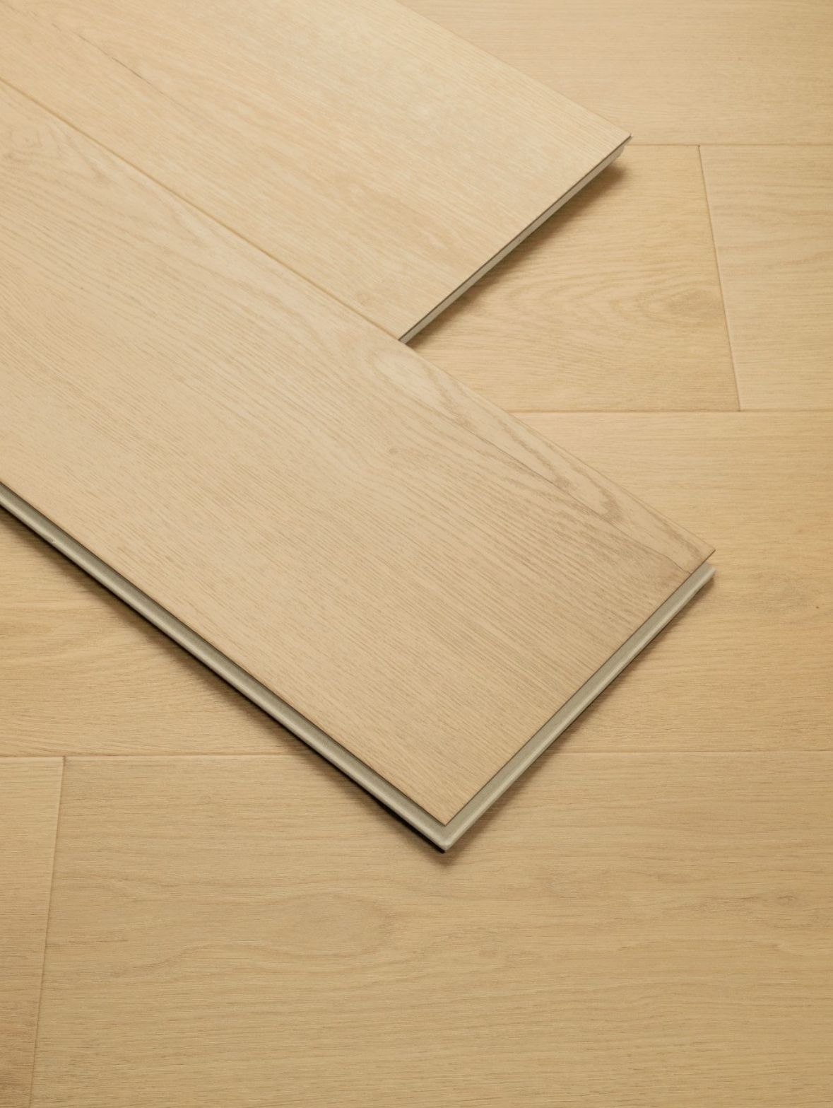 Wooden flooring planks, light beige color, stacked on each other, showing the interlocking edges.