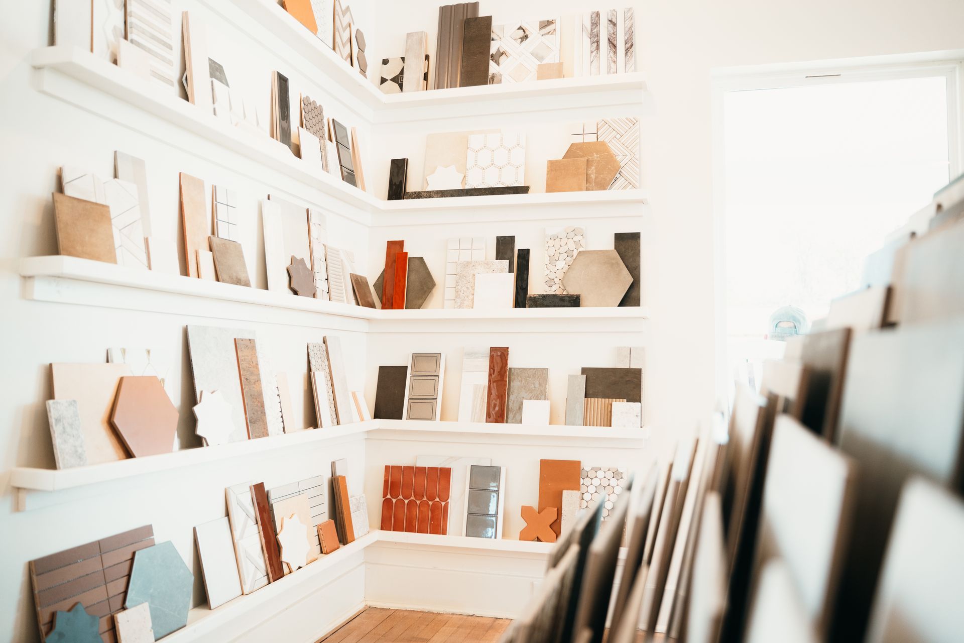 Tile samples displayed on white shelves in a bright showroom. Various shapes and colors are visible.