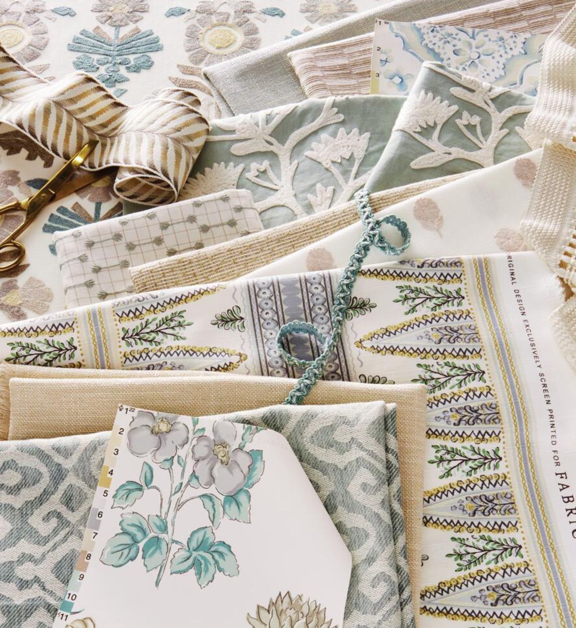 Pile of various textured fabric swatches in muted blues, greens, and beige, with floral and geometric patterns.