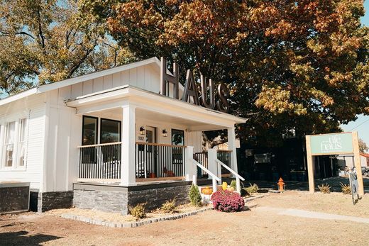 White building with porch, sign, and tree.