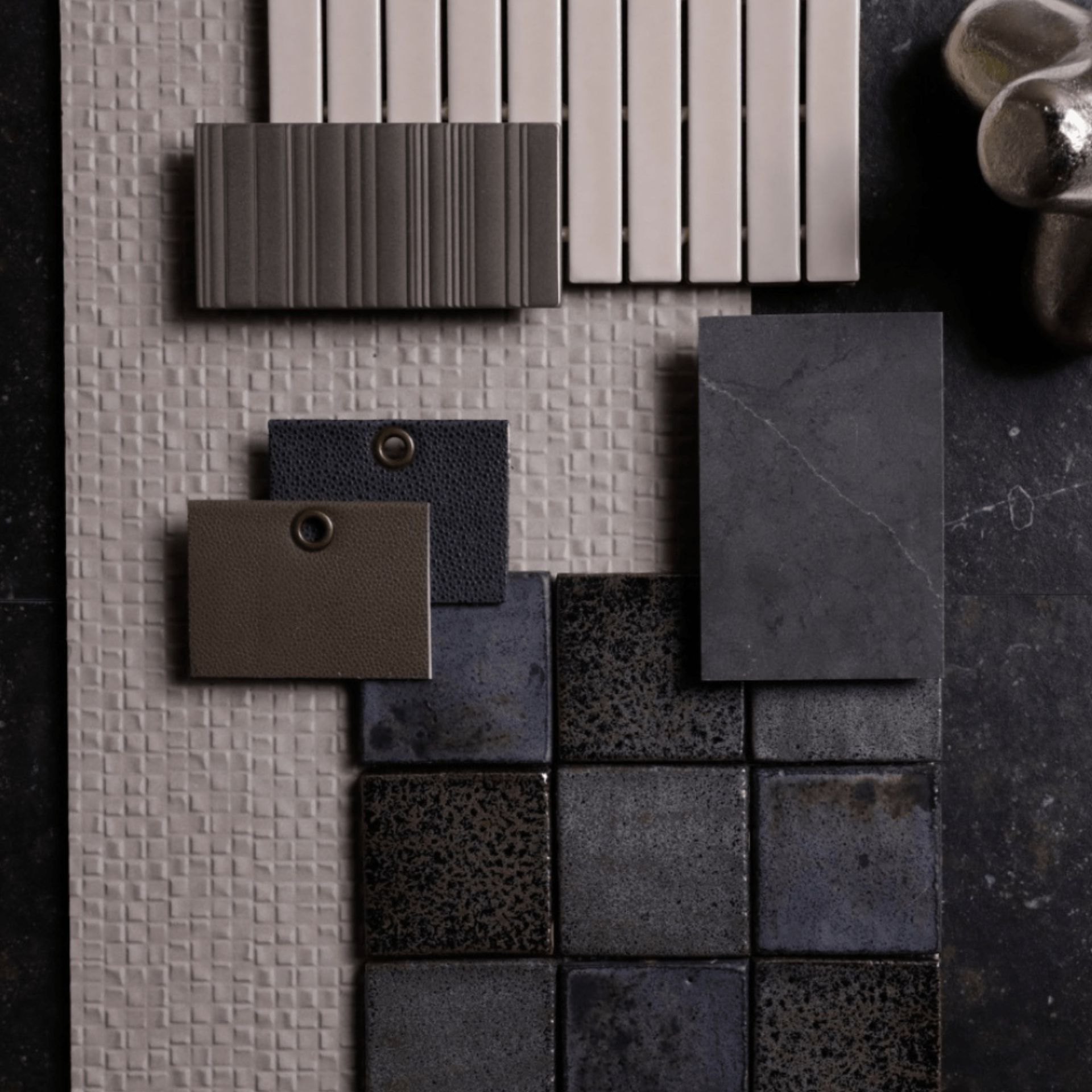 Mood board with various gray, blue, and beige textured tiles and metallic decor accents.