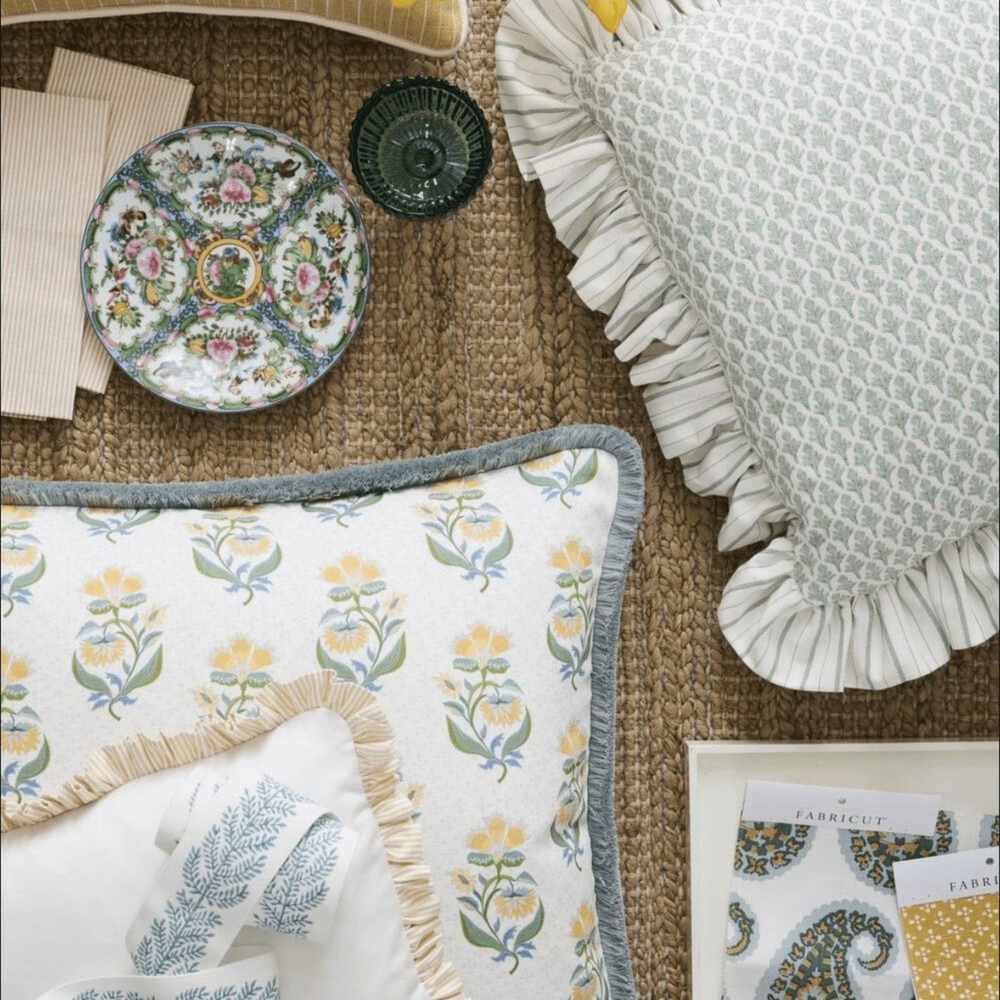 Arrangement of decorative pillows, plate, and fabric swatches in pastel colors on a brown woven rug.
