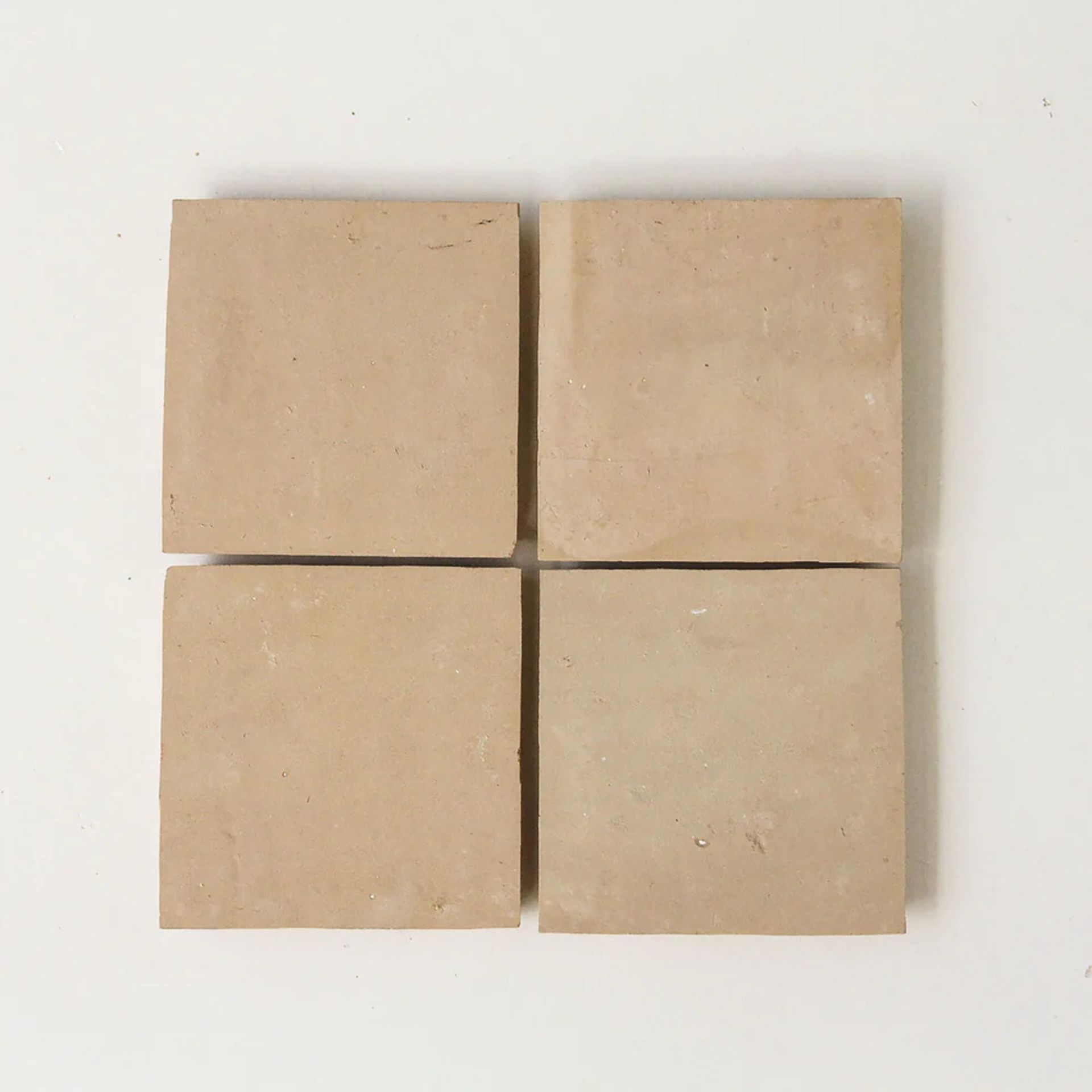 Four square beige tiles arranged in a square on a white background.