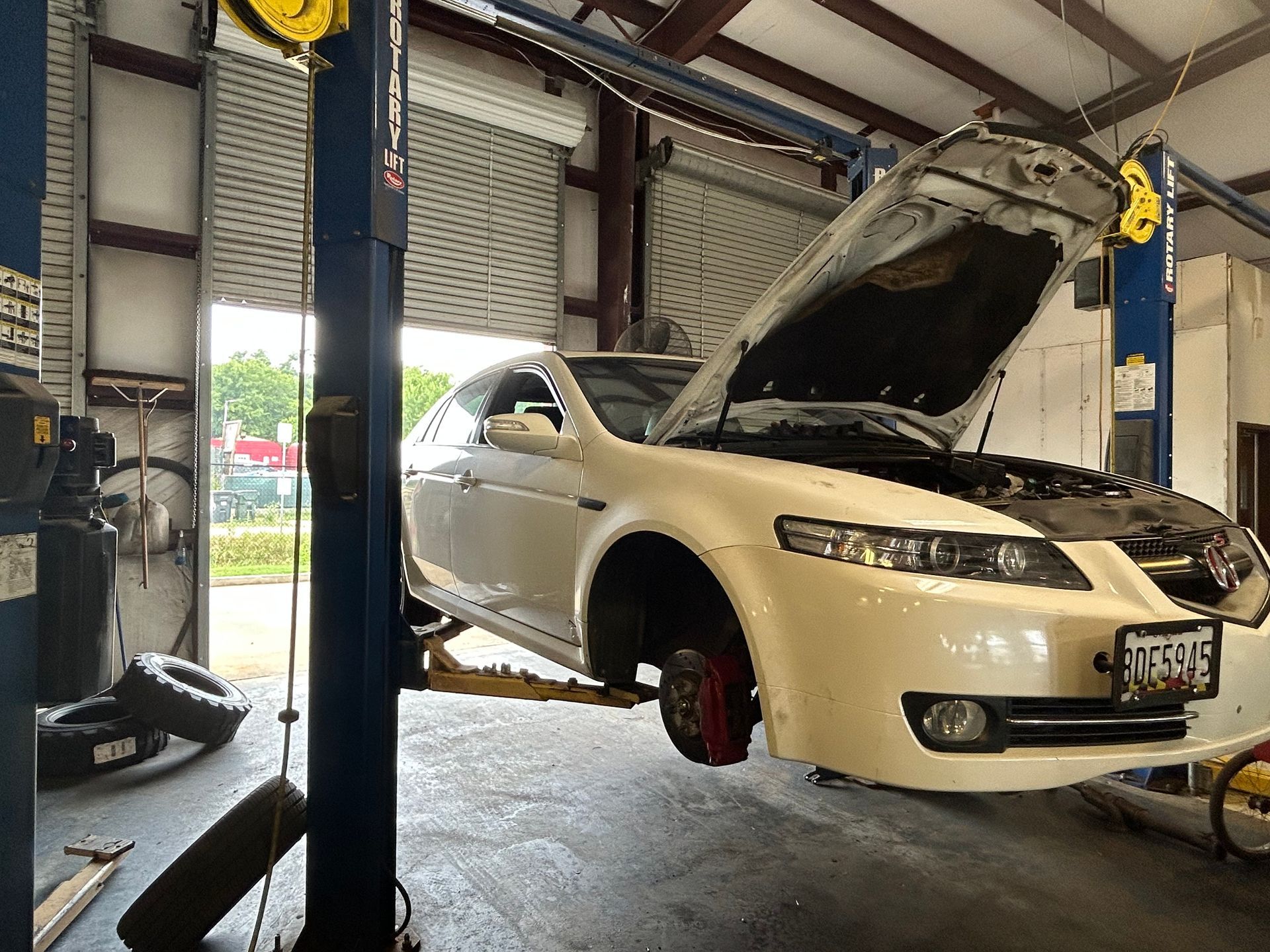 White car raised on a lift in a garage with the hood open, revealing engine parts.