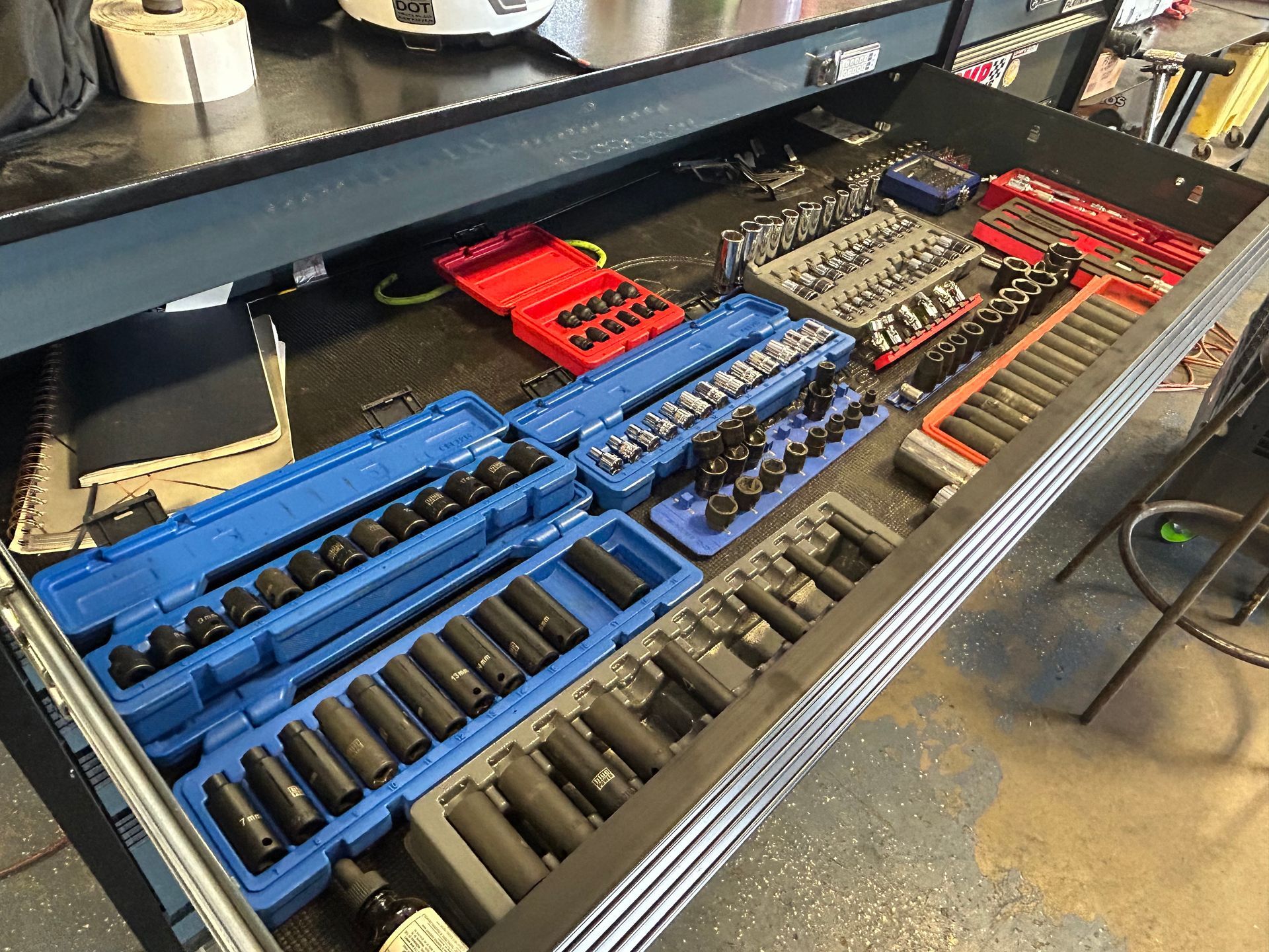 Open drawer of a tool chest filled with various sockets, organized in blue and red cases.