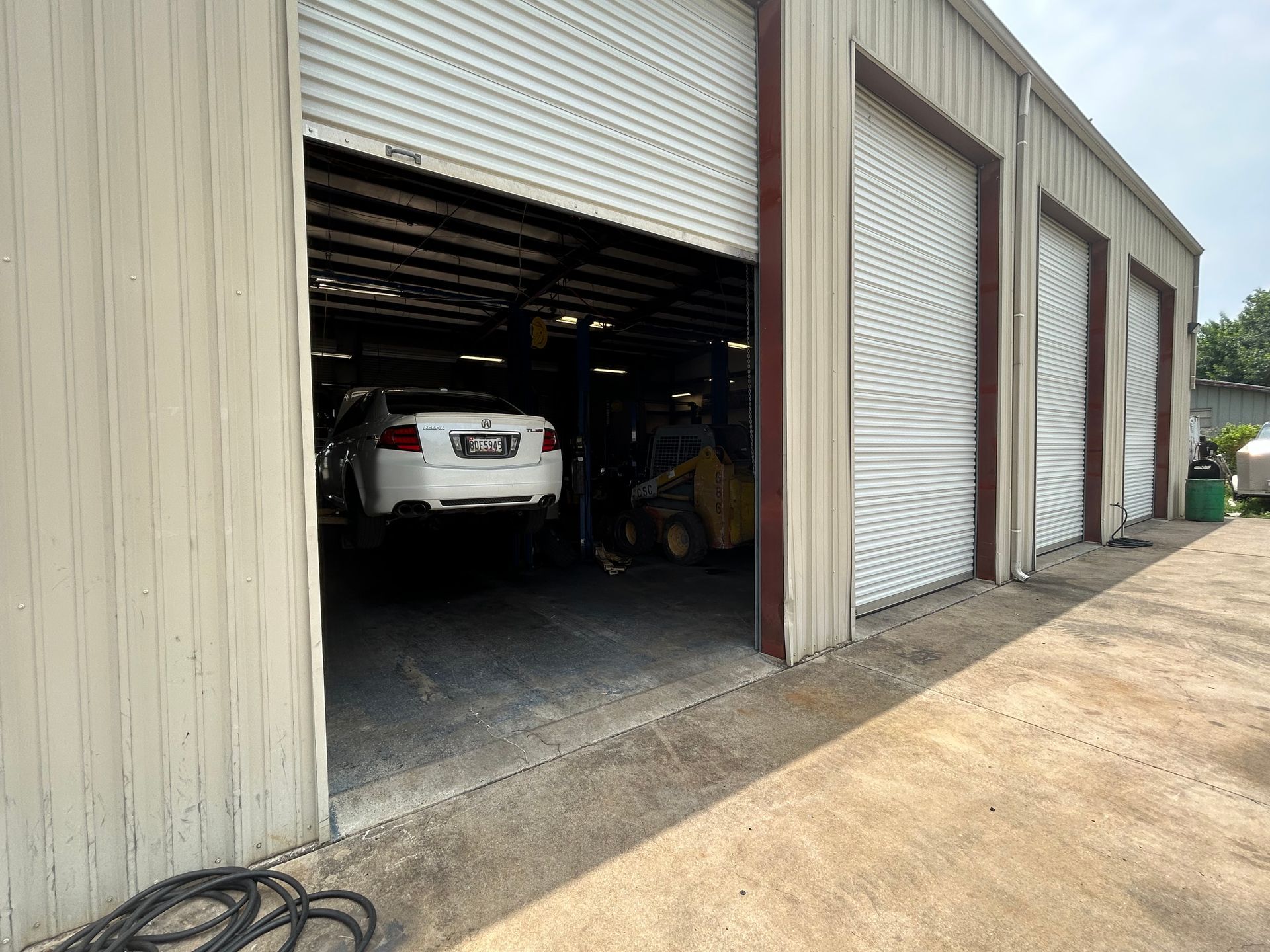 Exterior view of a garage with three bays; one bay open, showing a white car inside.
