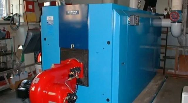 Blue industrial boiler with a red burner in a basement setting.