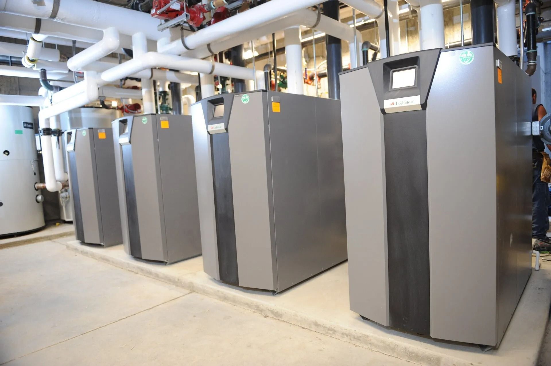 Row of gray industrial heating units with white pipes in a building.