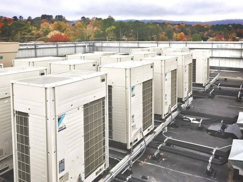 White HVAC units on a flat roof with autumn trees in the background.
