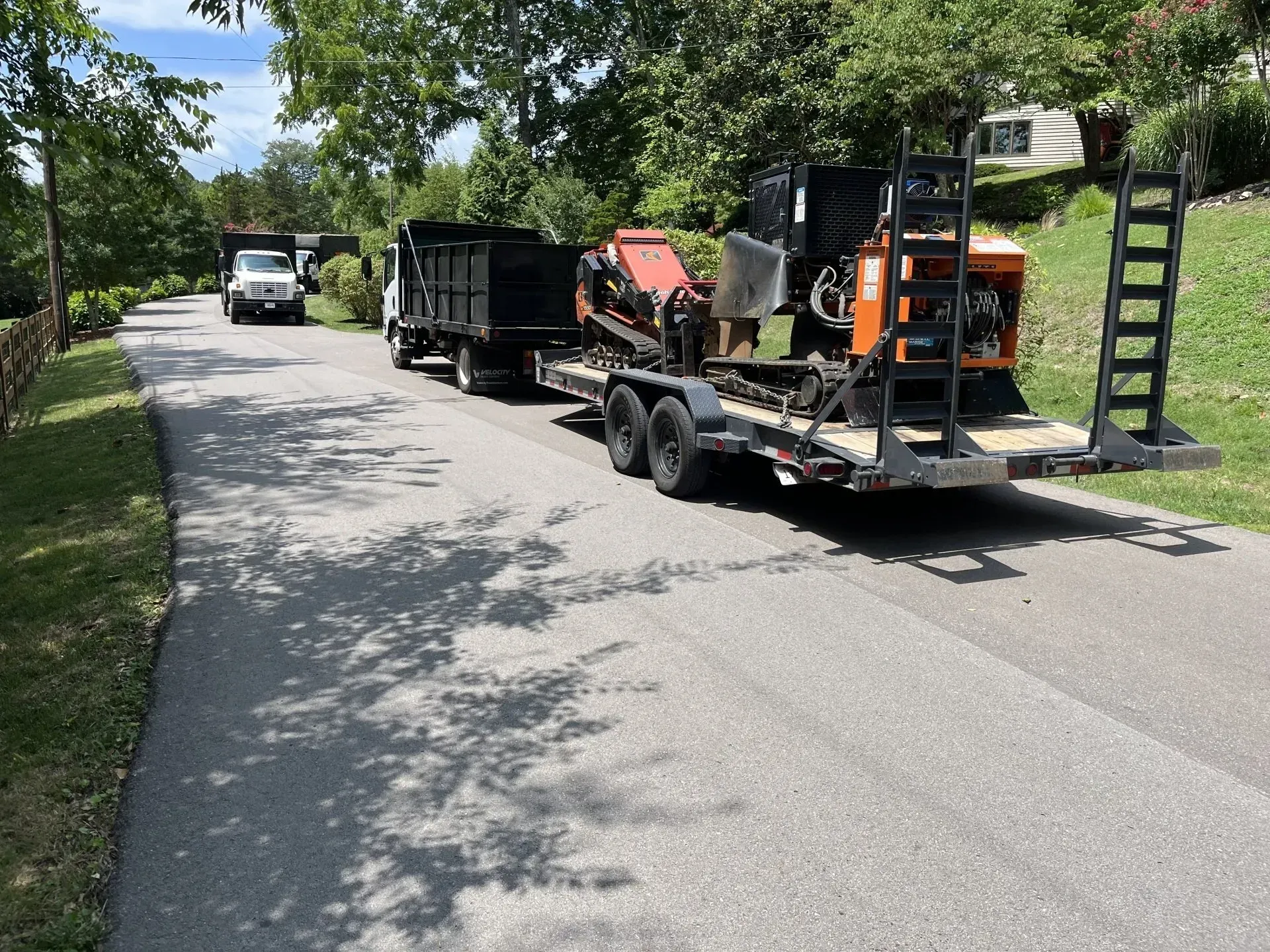 Truck pulling a trailer with equipment; parked on asphalt road. A truck is in the distance. Sunny day.
