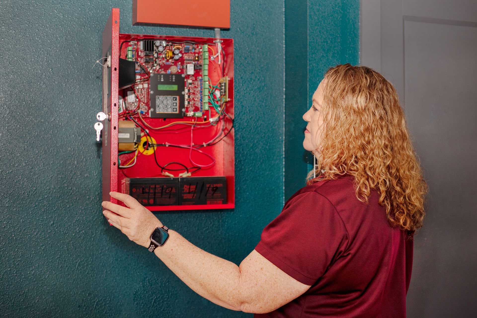 A woman is working on a fire alarm system on a wall.