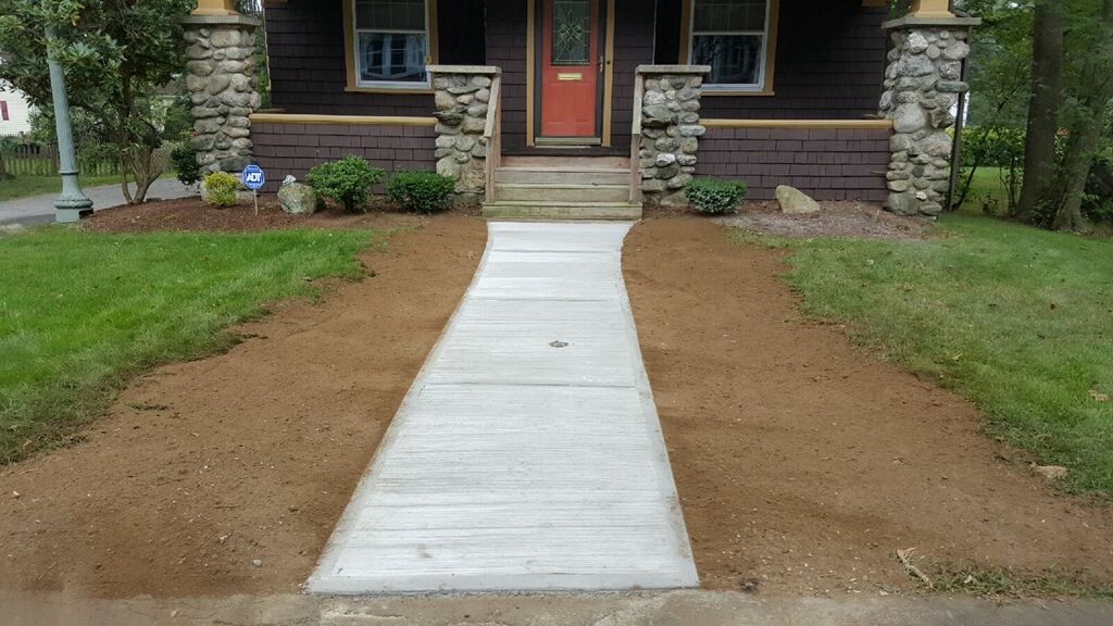 A concrete walkway leading to a house with a red door