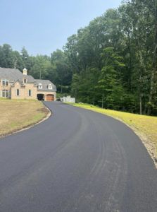 A house is sitting on the side of a curvy road surrounded by trees.