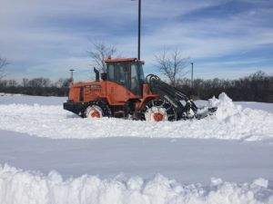 A bulldozer is clearing snow from a parking lot.