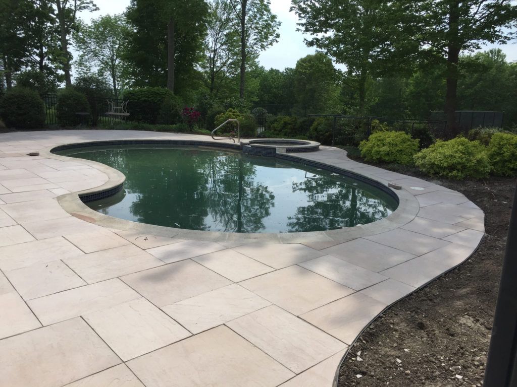 A large swimming pool is surrounded by a patio and trees.