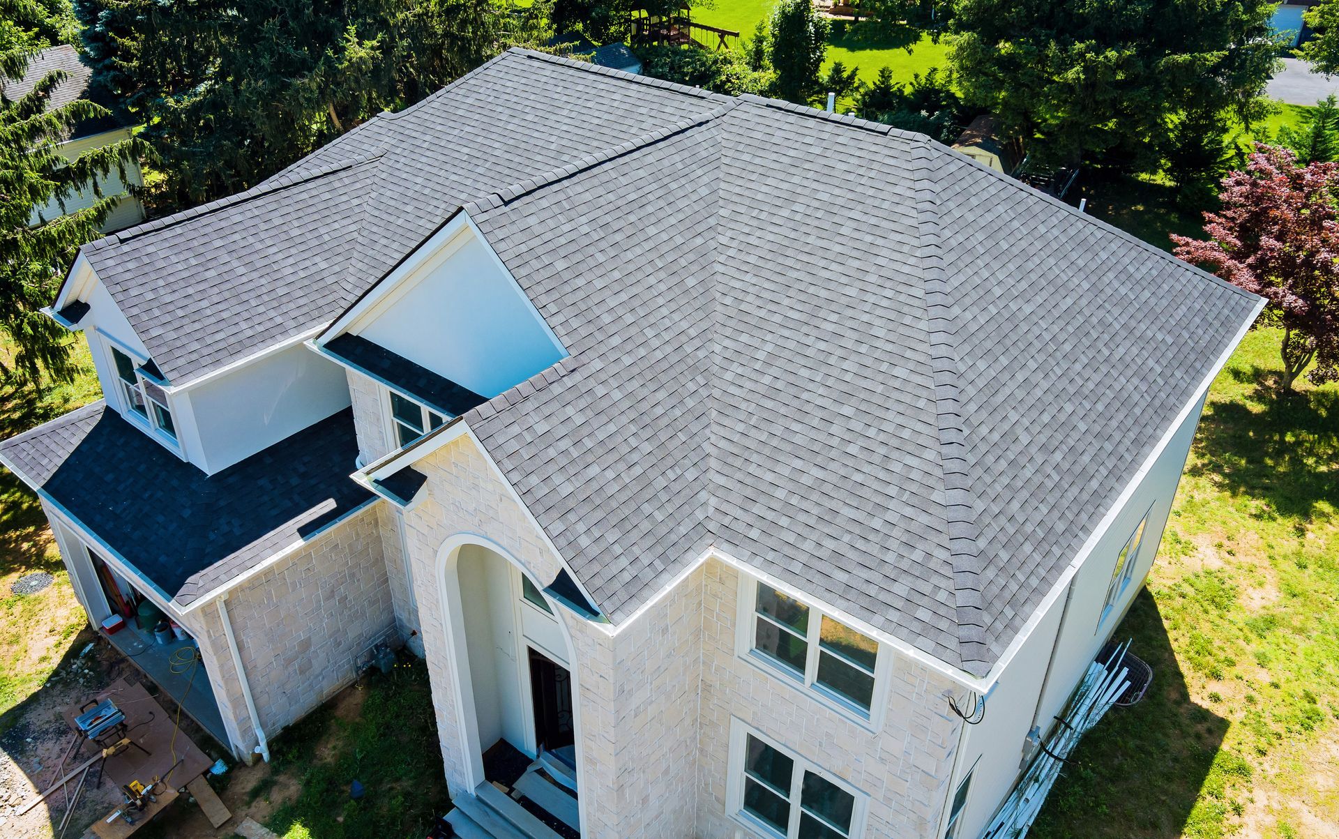 Two-story house with dark gray asphalt shingle roof. Off-white exterior, surrounded by green grass and trees.