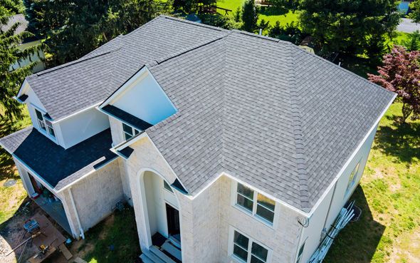 Drone view of a two-story house with a dark gray shingled roof, beige siding, and white trim.