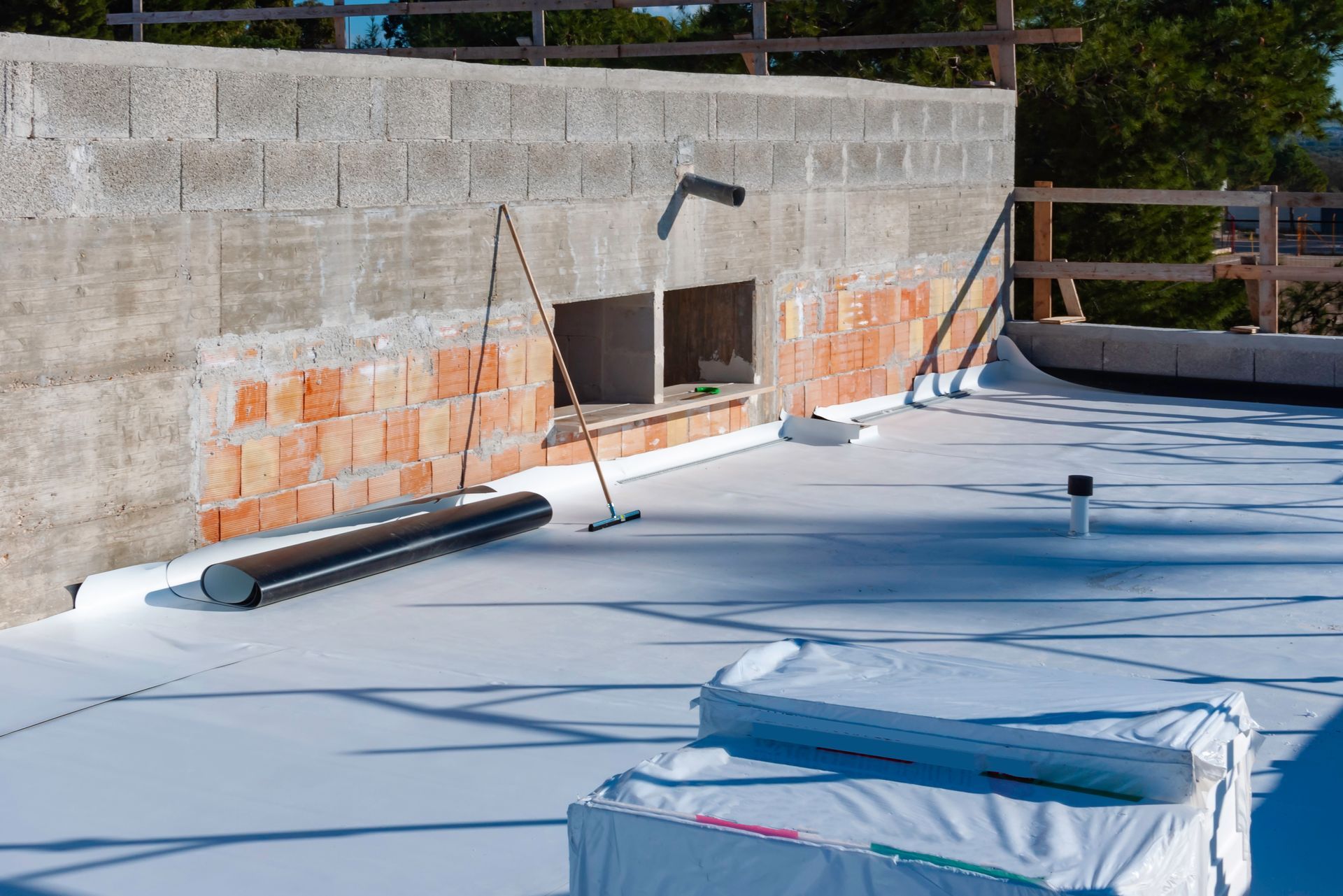 Flat roof under construction; white membrane laid, adjacent brick and concrete block wall.