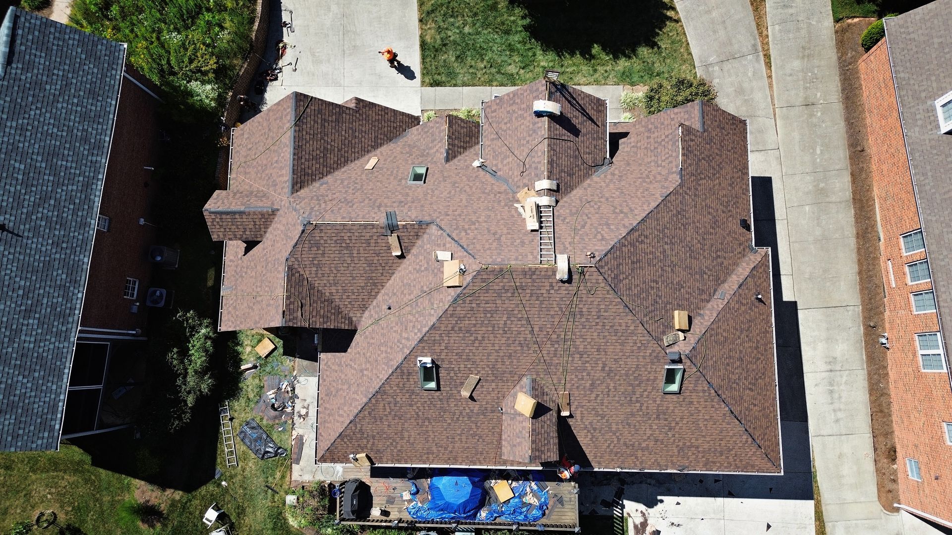 Aerial view of a brown roof with construction activity, including tools and a blue tarp, on a sunny day.