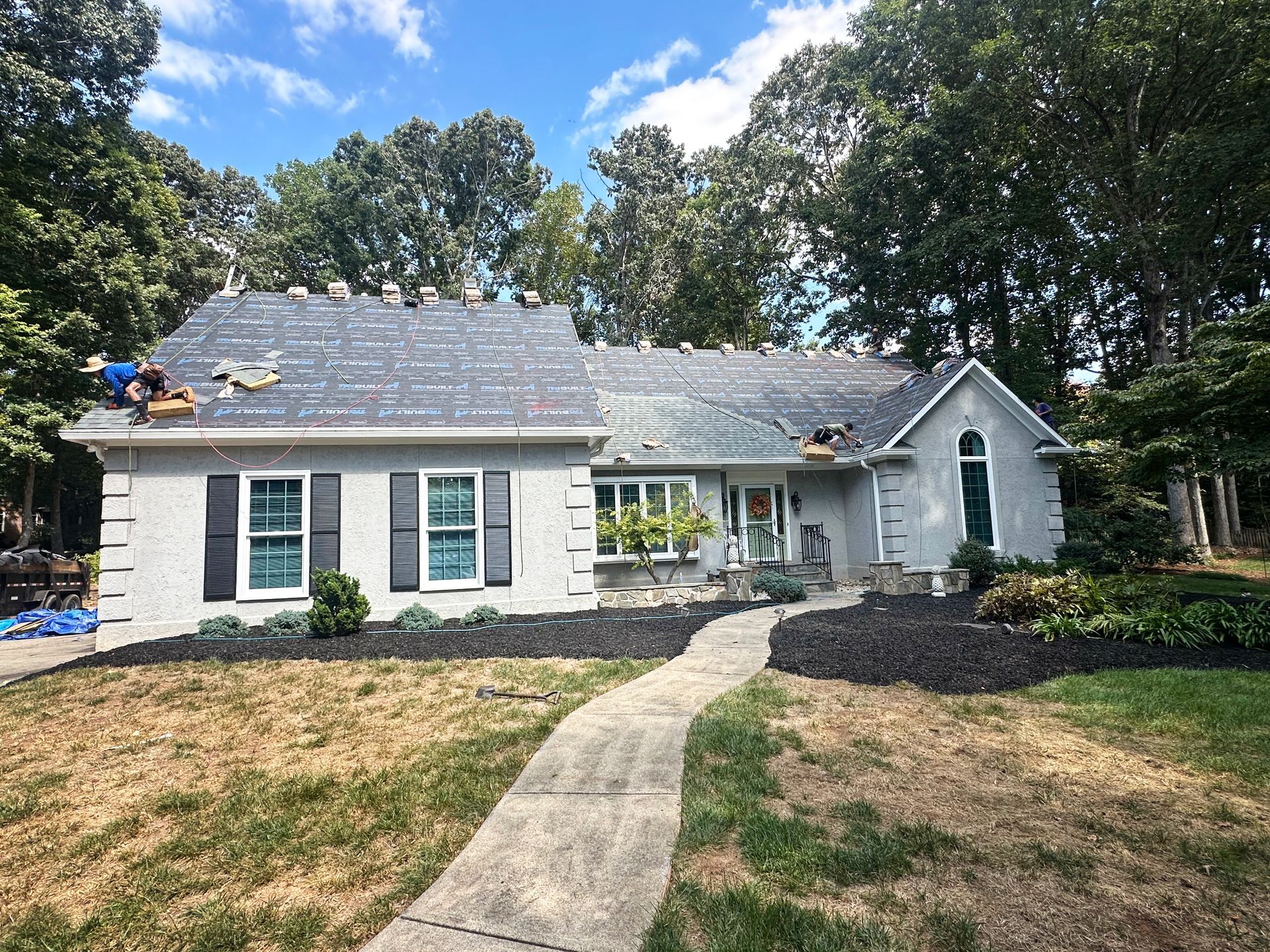 House under roof repair with workers on the roof, trees, and blue sky.