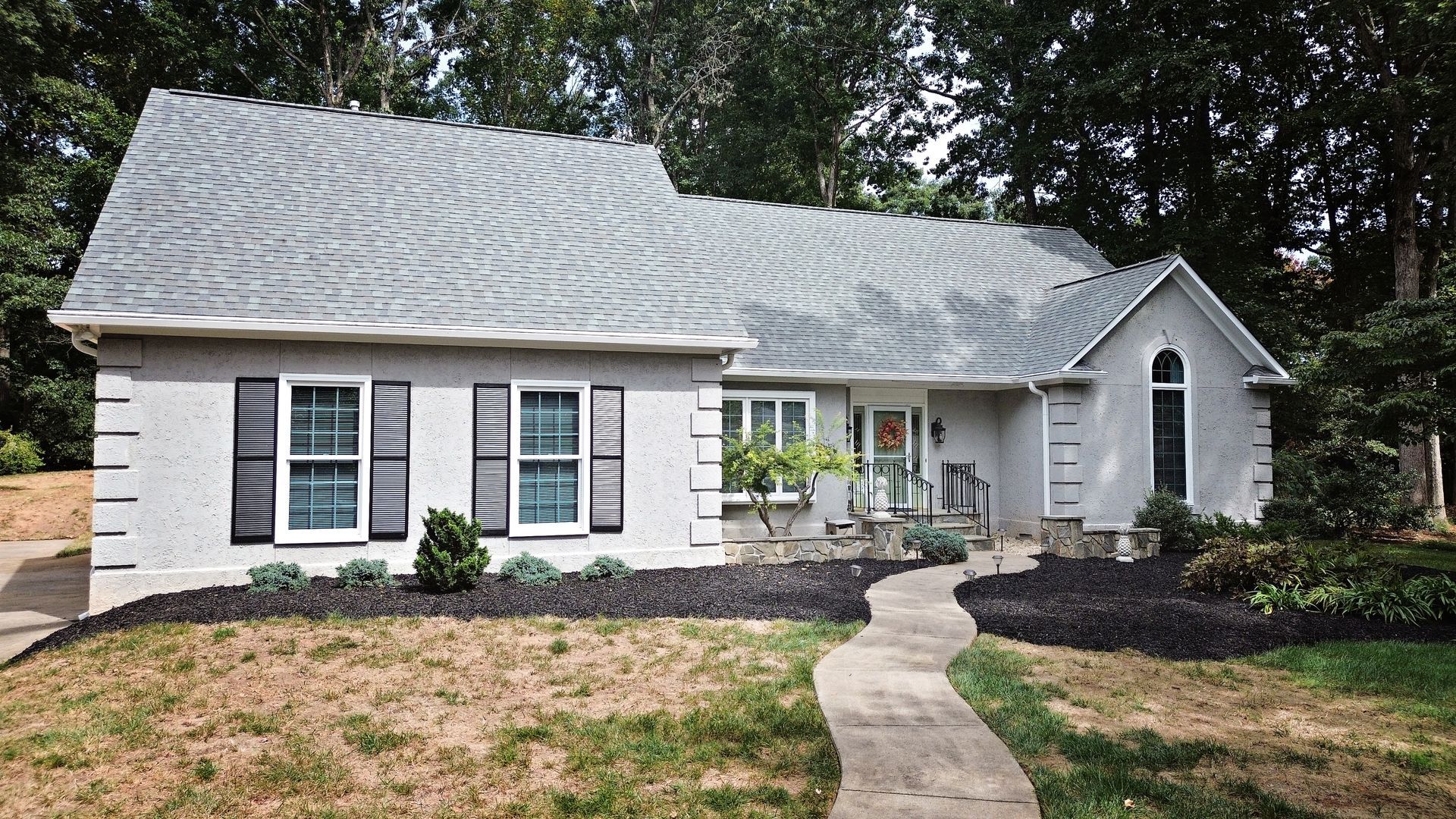 Gray stucco house with gray roof, black shutters, and winding walkway.
