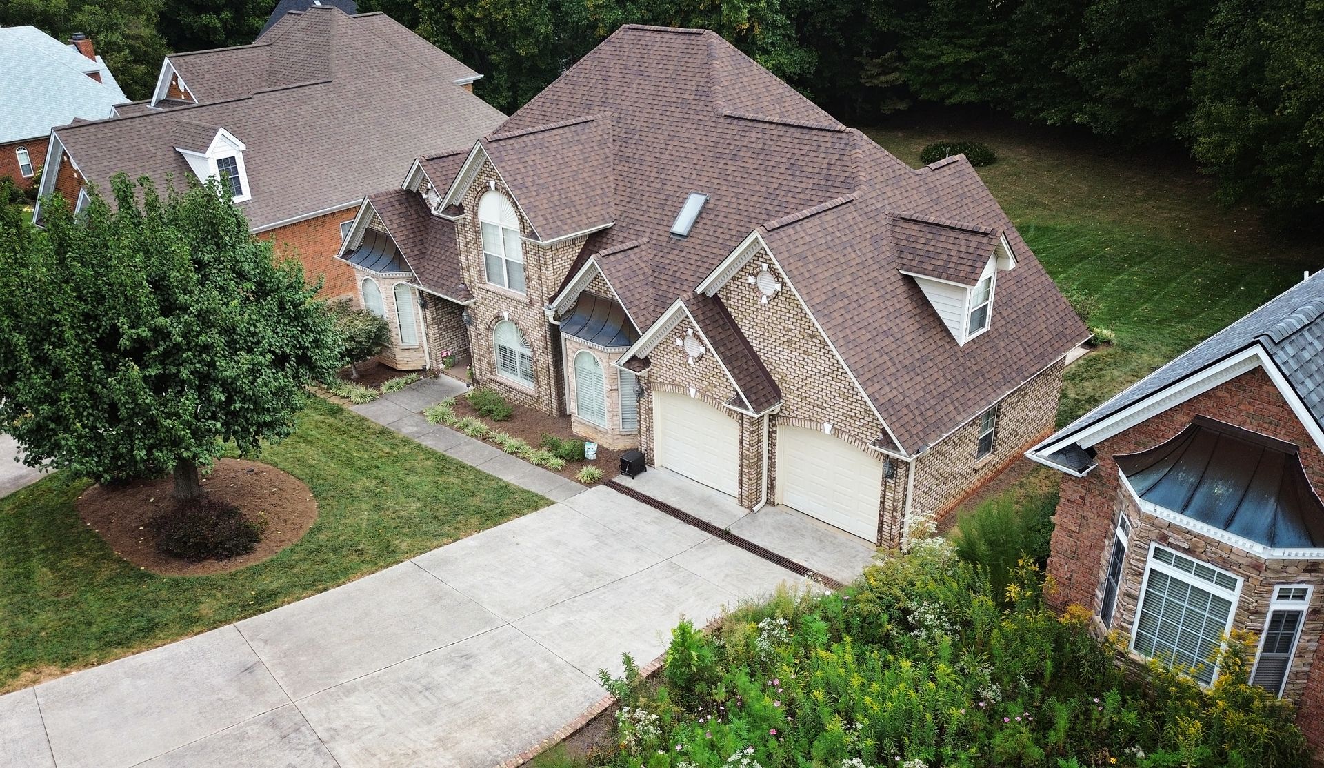 Suburban house with stone and brick exterior, two-car garage, and brown roof. Green lawn and trees.