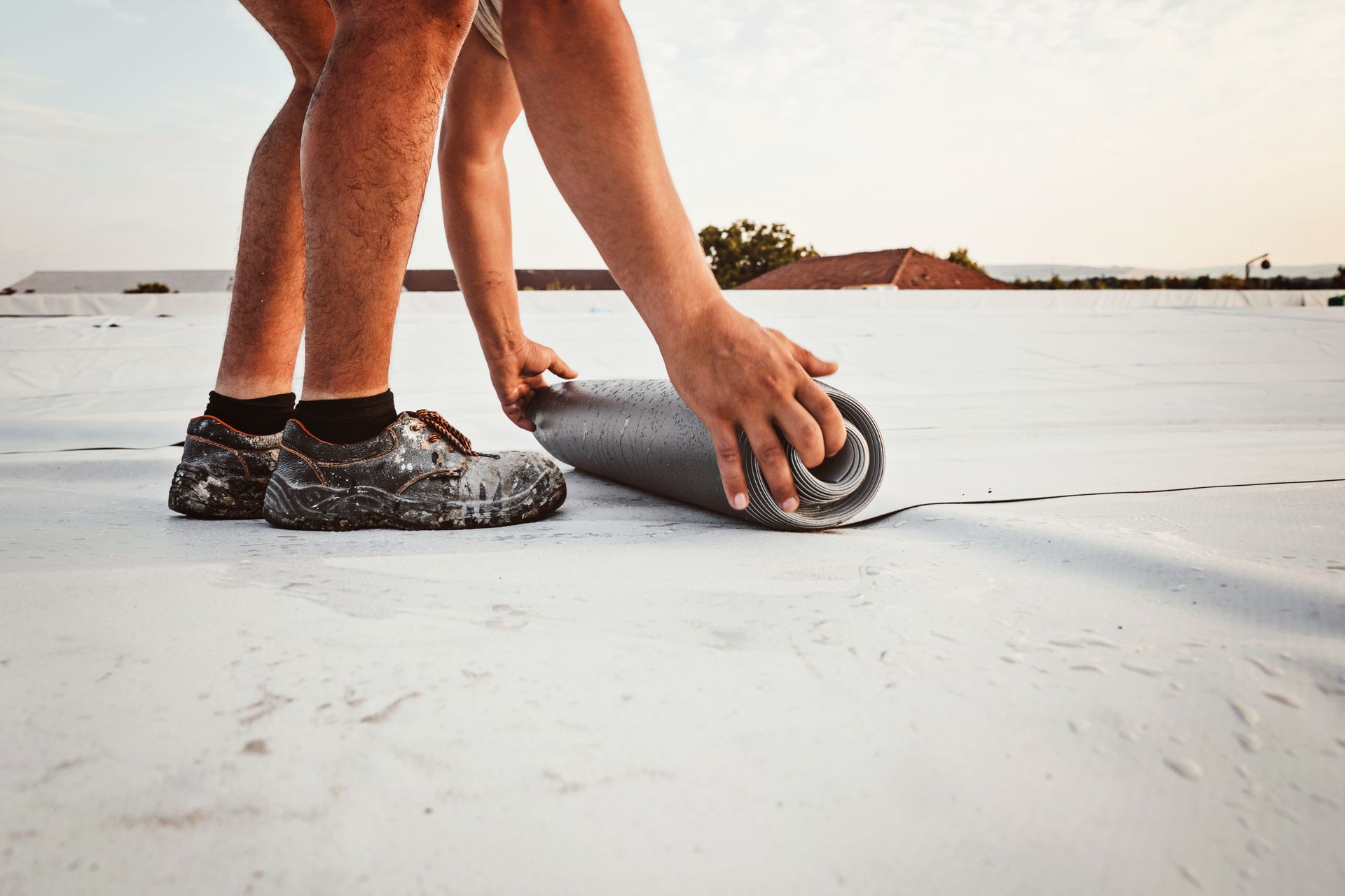Person rolling out a gray roofing membrane on a flat white roof.