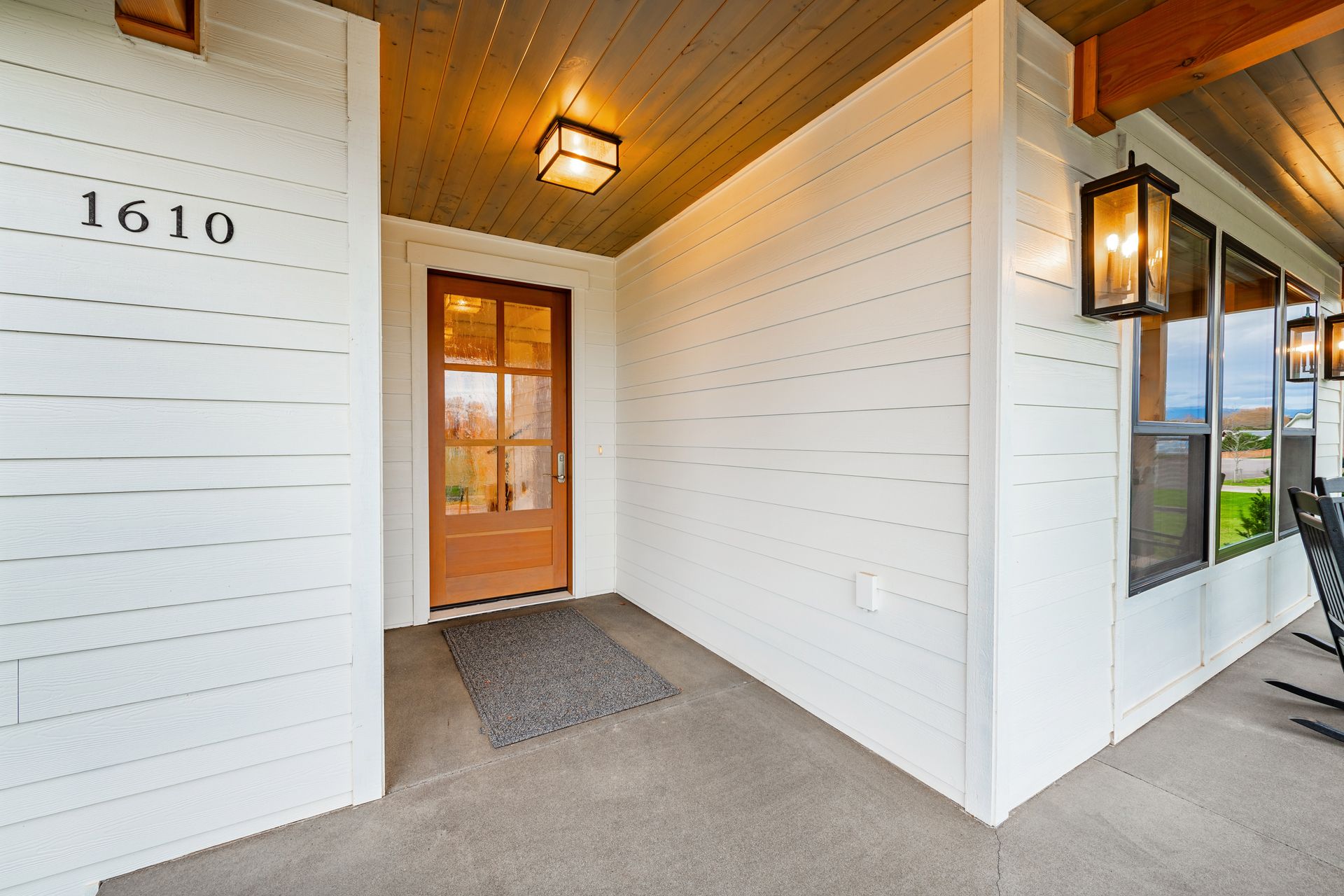 Exterior of a house entrance with brown door, white siding, and porch lights. The address 1610 is visible.