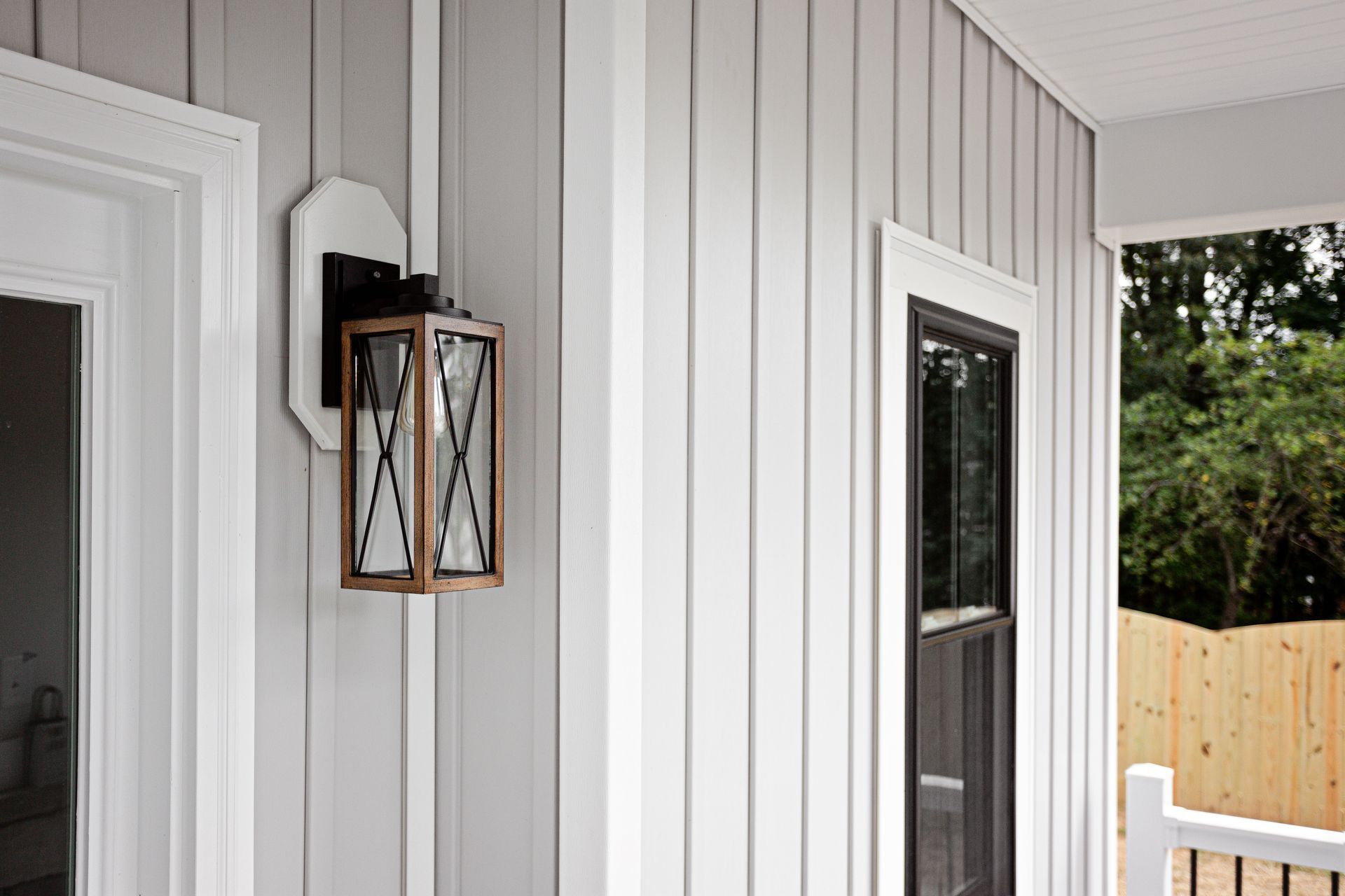 Exterior wall with gray vertical siding, white trim, and a decorative lantern.