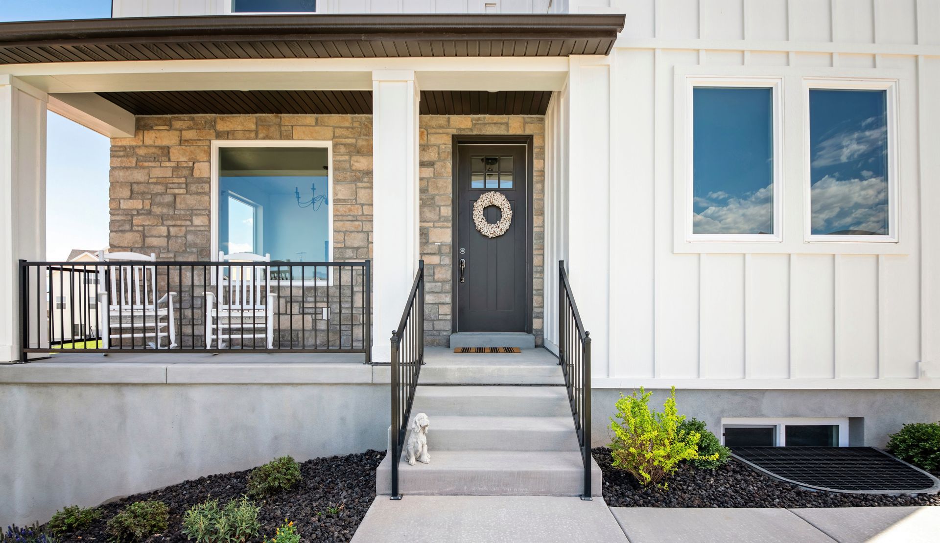 White house exterior with porch, steps, dark door with wreath, windows reflecting blue sky.