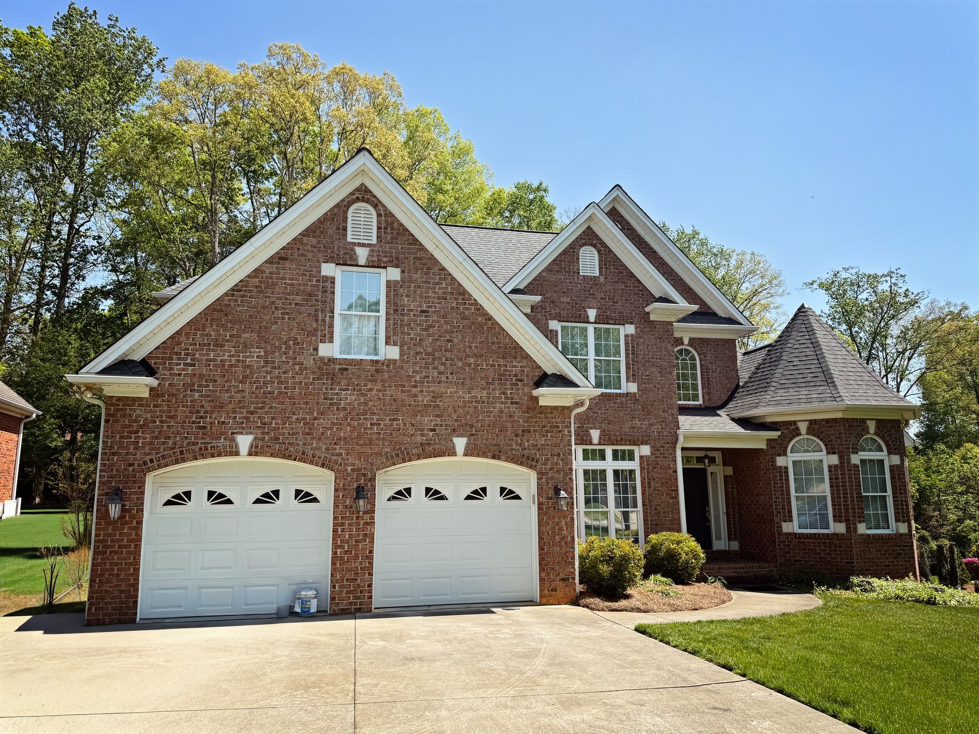 Two-story brick house with white garage doors and a circular tower, set on a green lawn with trees.