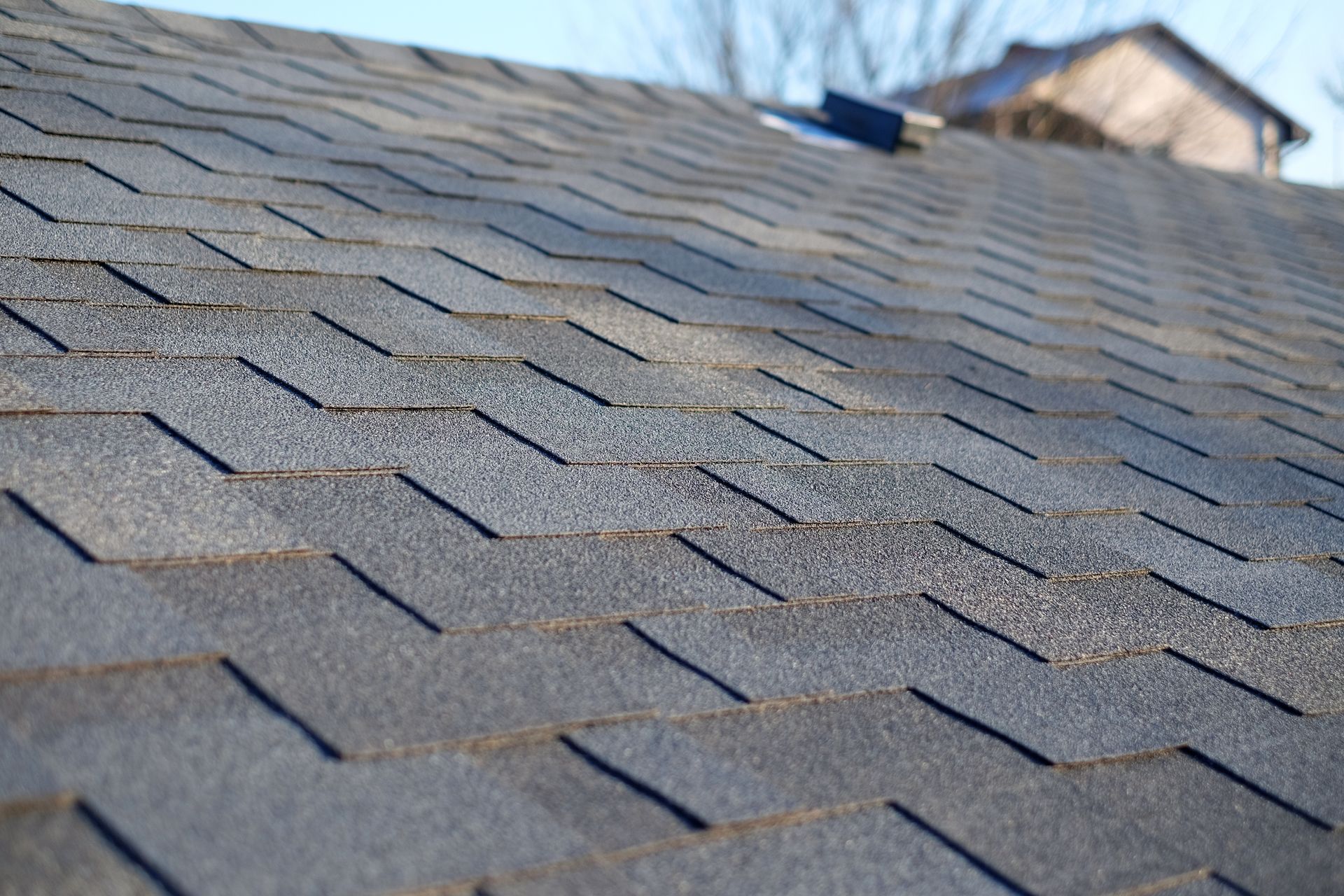 Close-up of a weathered asphalt shingle roof, angled view under a clear sky.