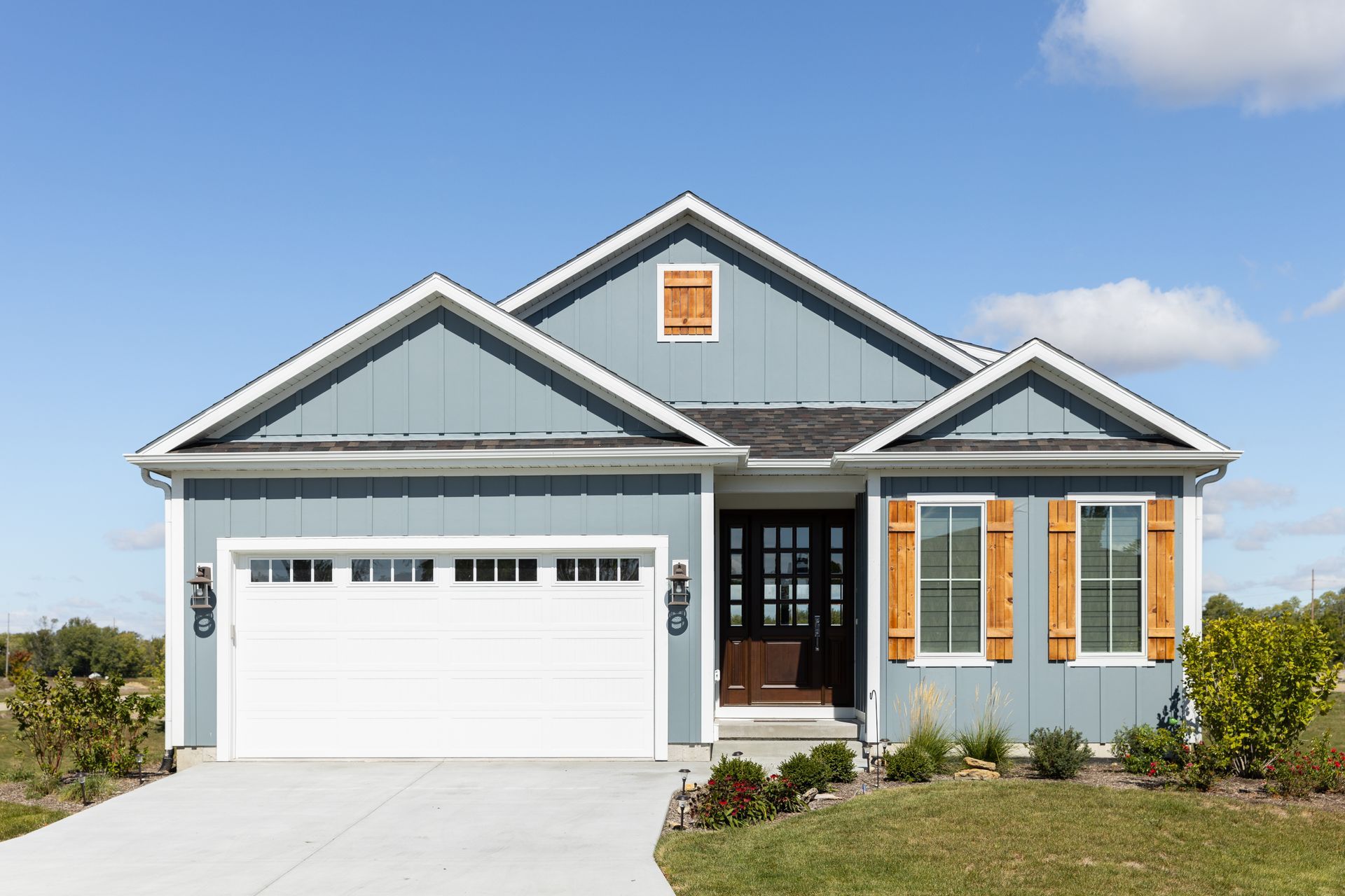 Blue siding ranch-style house with white garage door and brown front door, sunny day.