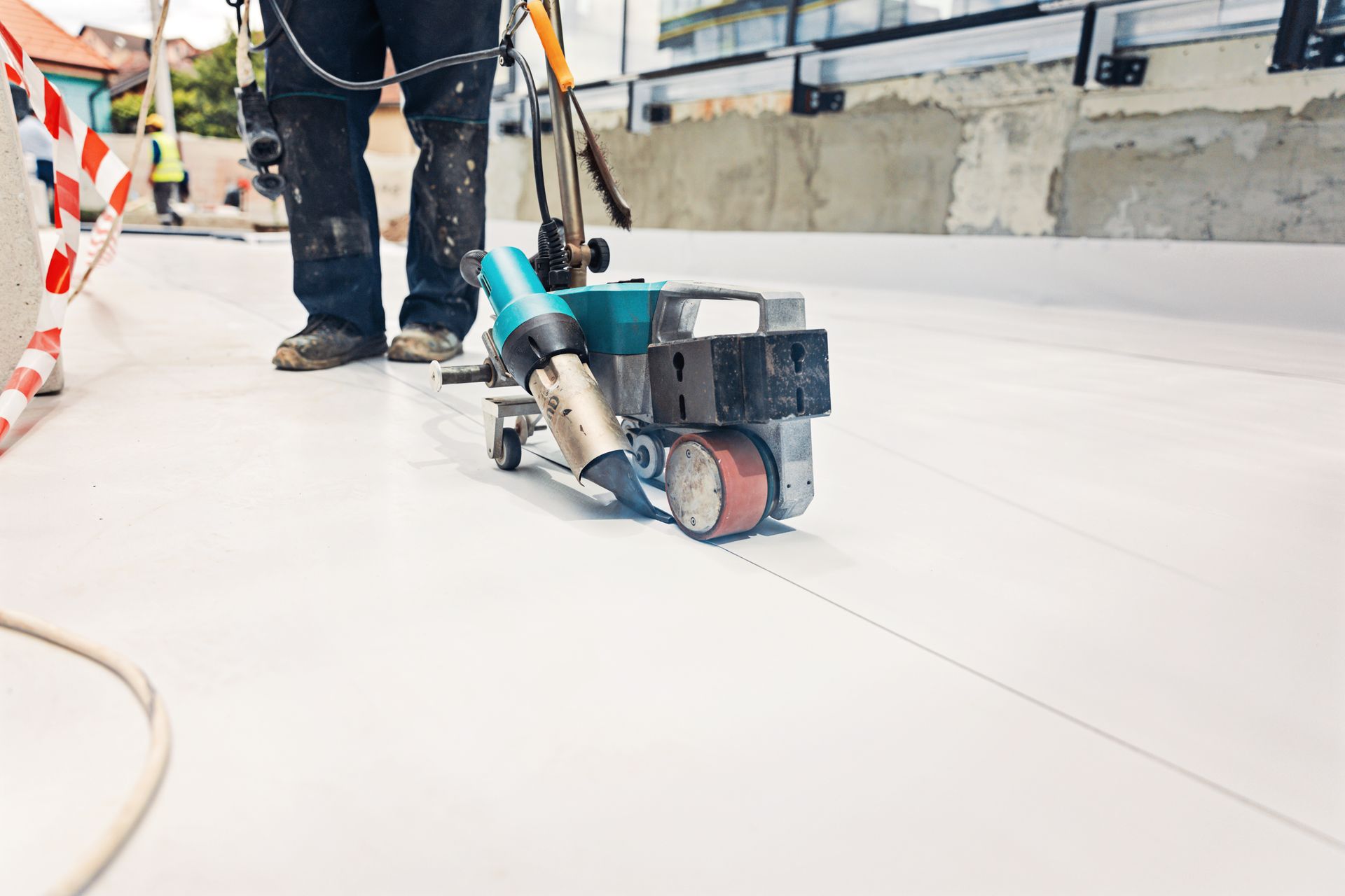 Roofer using a welding machine to seal white roofing material seams on a building.