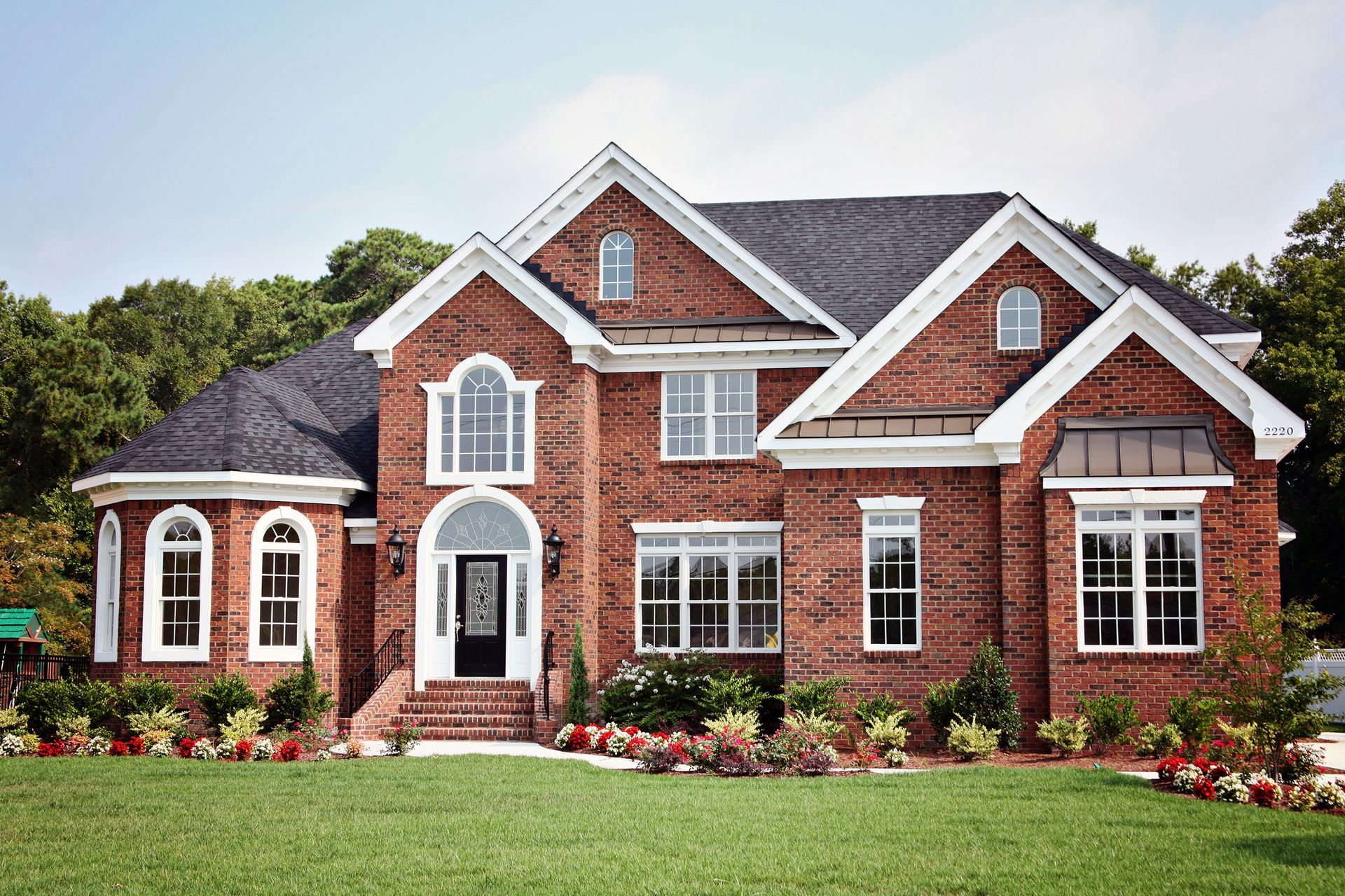 Red brick house with white trim, arched windows, and a black front door on a green lawn.