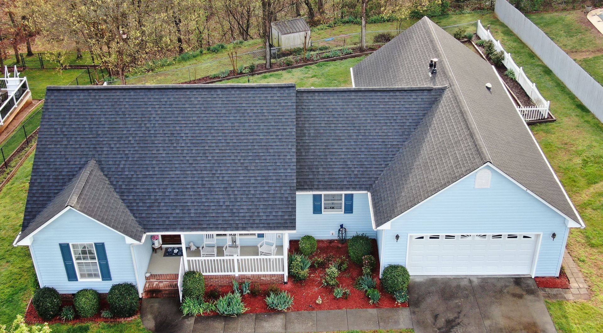 Blue house with black roof, white trim, and a red mulch landscaping.