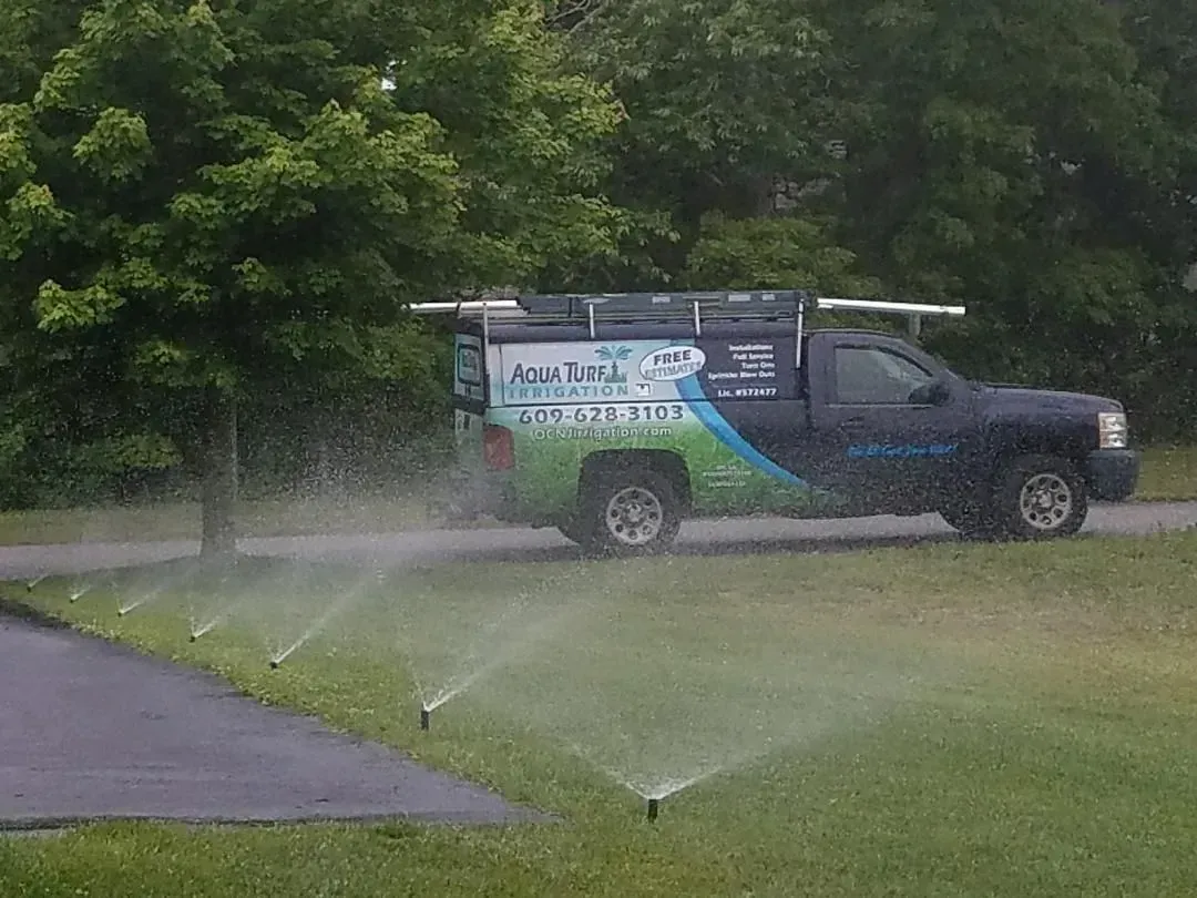 Sprinkler system watering a lawn beside a road with a service truck parked nearby.