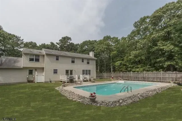 Two-story beige house with a pool in the backyard surrounded by a stone border.