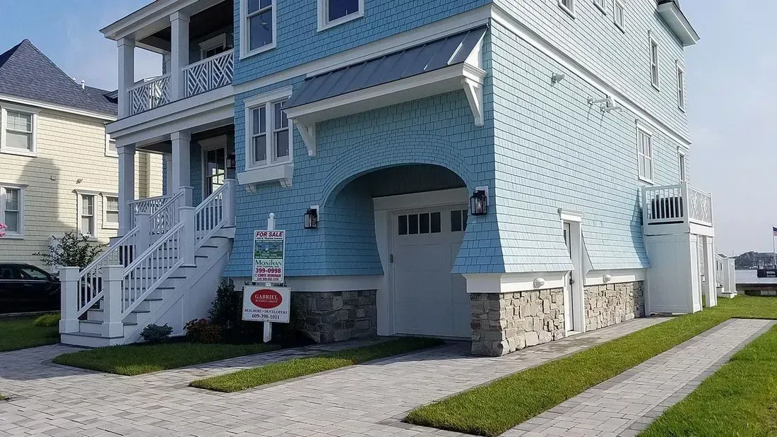 Blue house with white trim, stone foundation, and driveway.